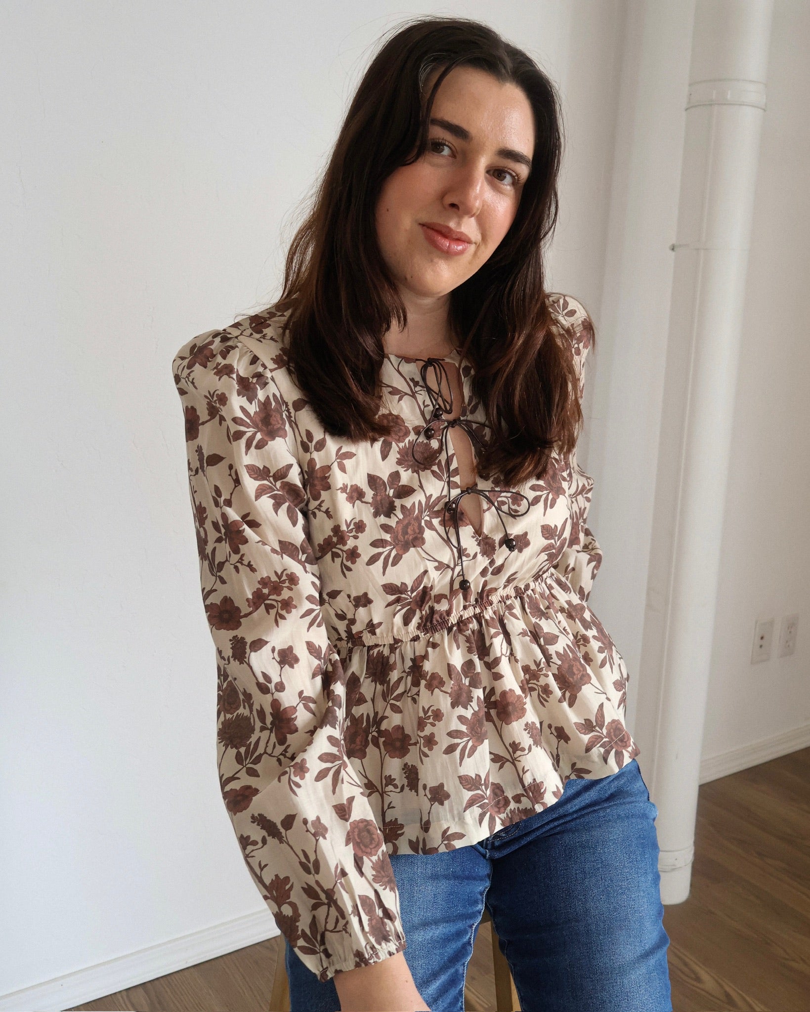 Woman wearing a floral blouse and blue jeans indoors.