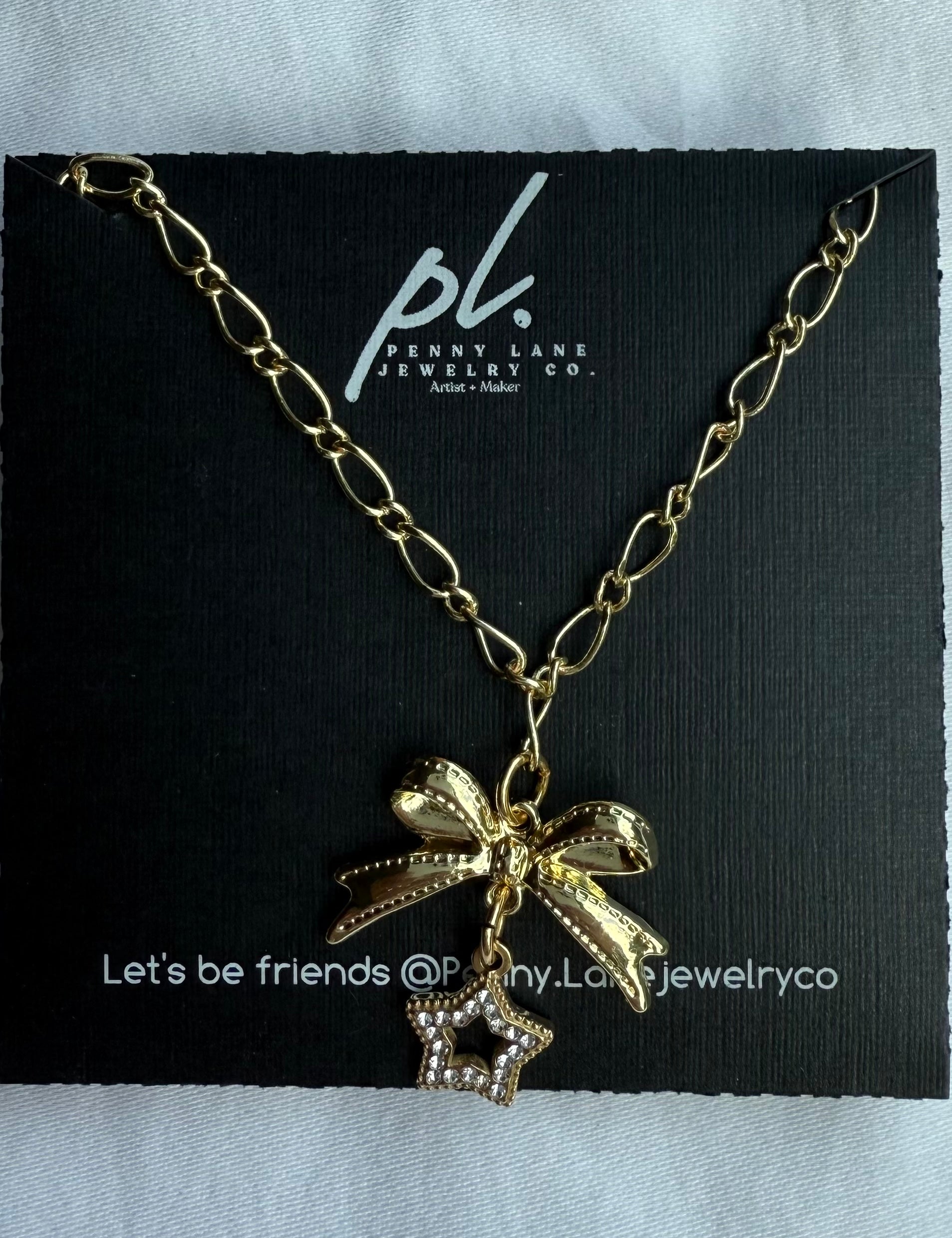 Gold necklace with bow and star charm on a Penny Lane Jewelry Co. card.