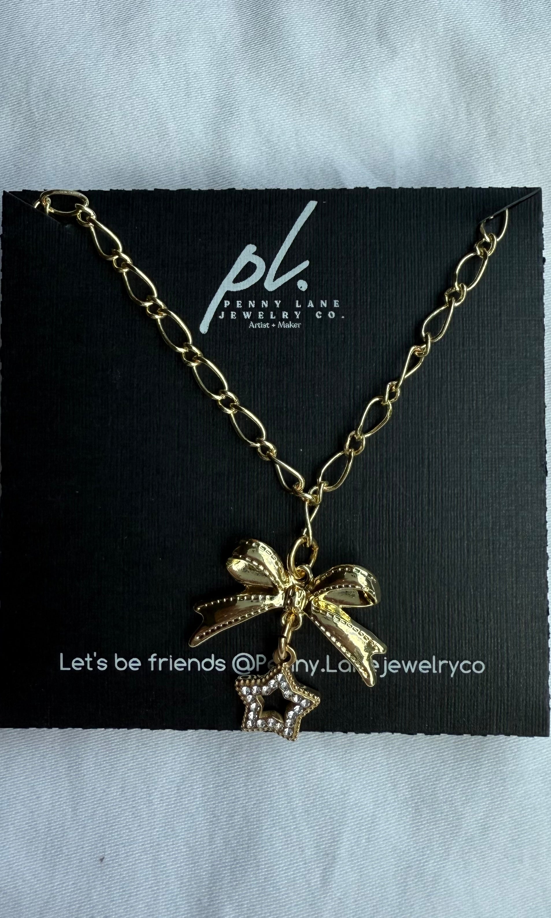 Gold necklace with bow and star charm on a Penny Lane Jewelry Co. card.