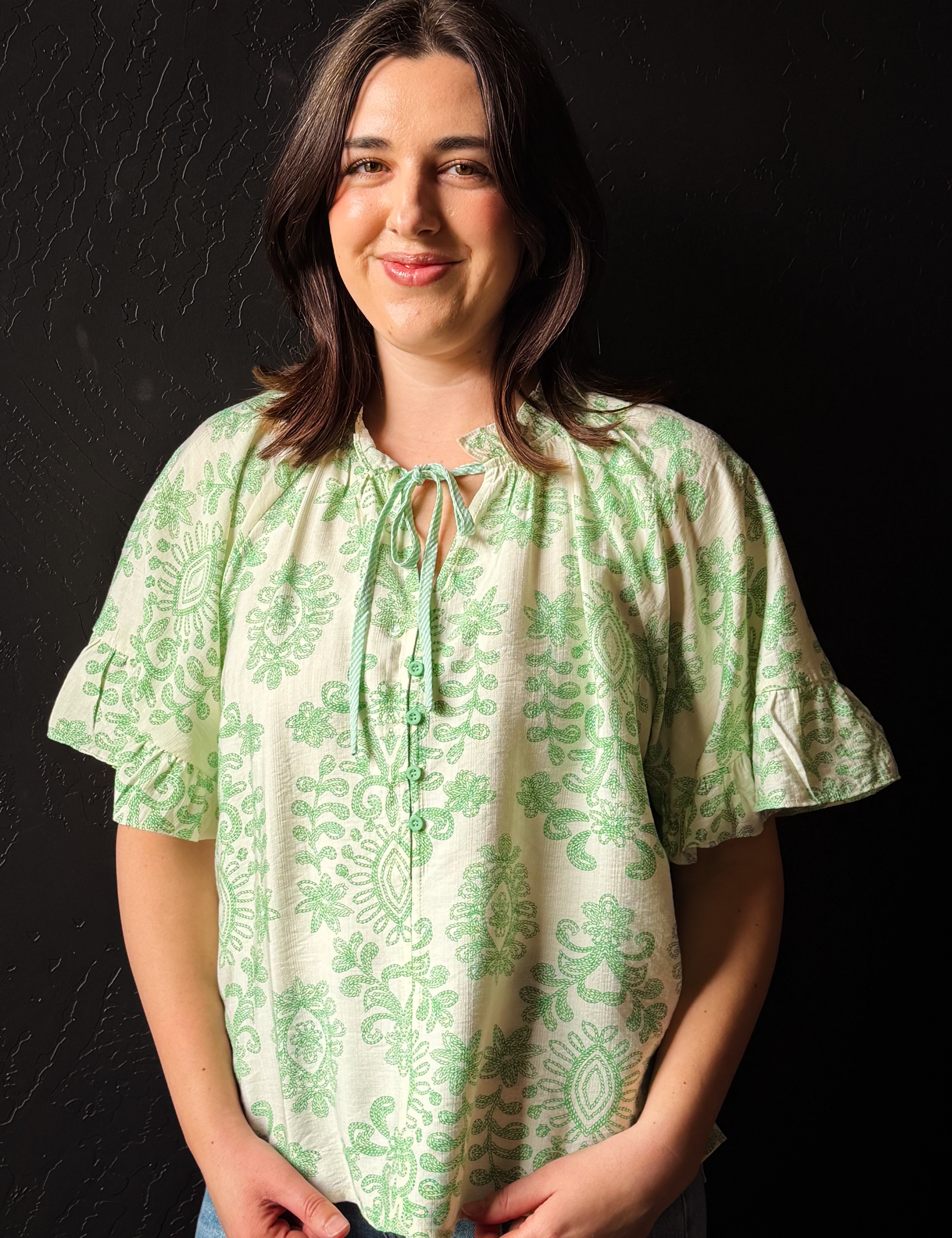 Woman wearing a green patterned blouse against a black background
