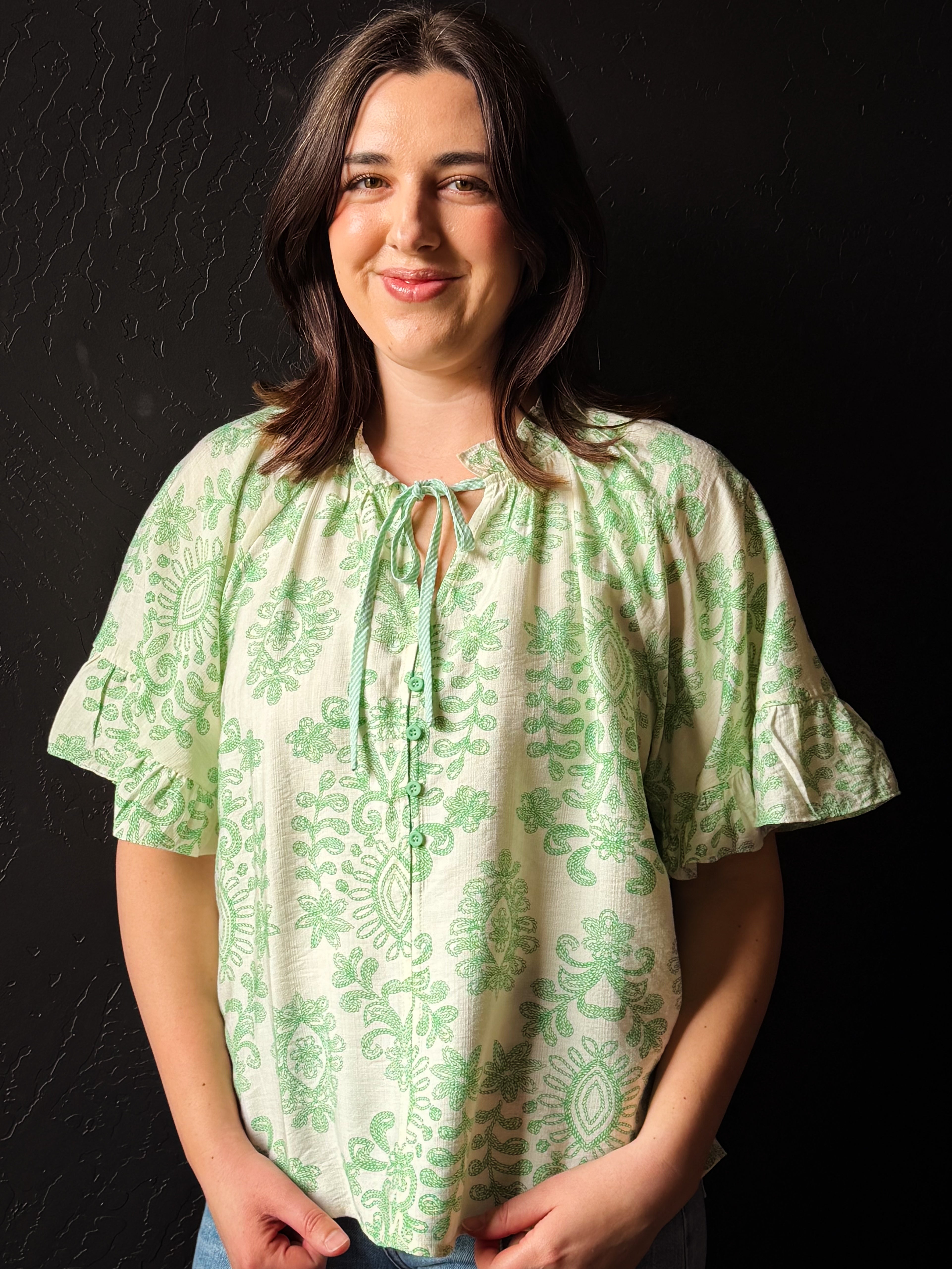 Woman wearing a green patterned blouse against a black background
