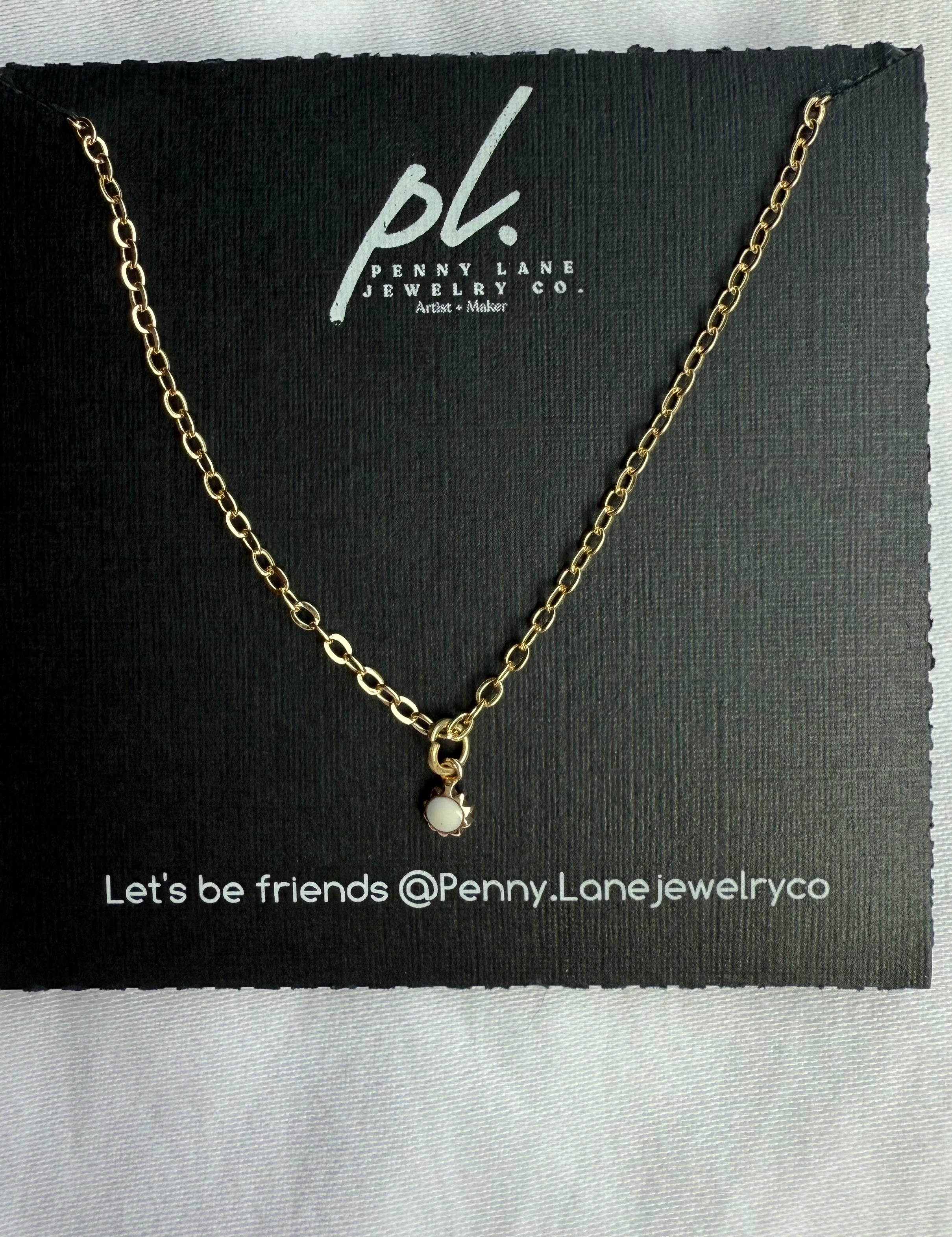 Gold necklace with a small pendant on a Penny Lane Jewelry Co. card.