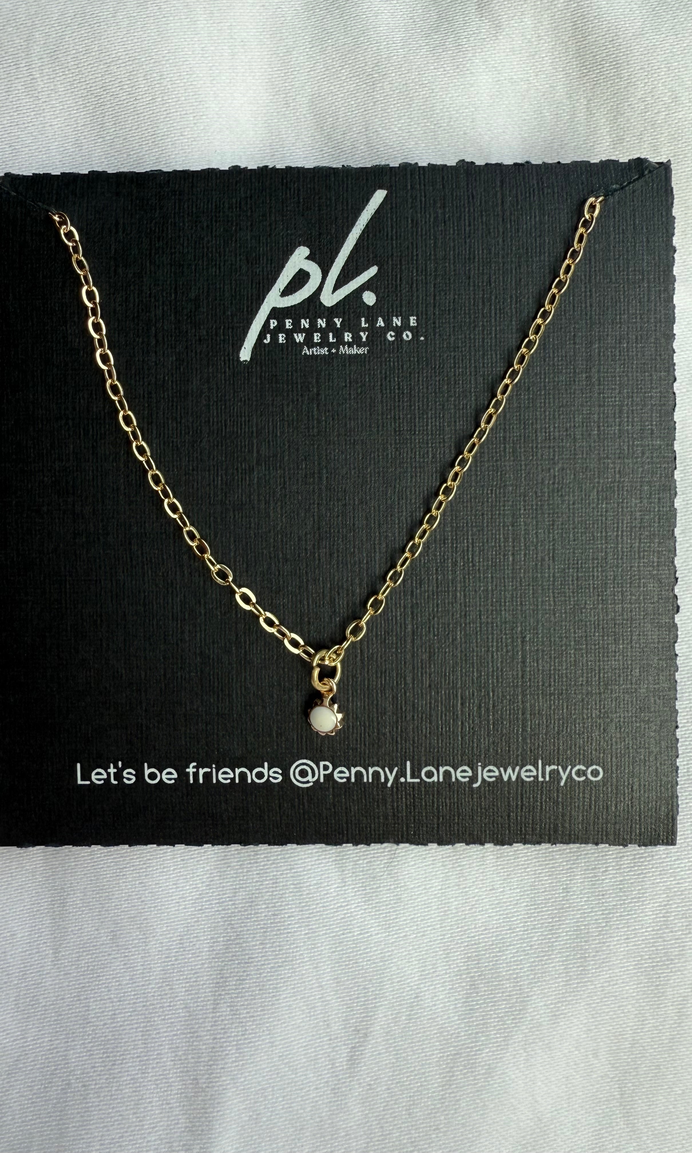 Gold necklace with a small pendant on a Penny Lane Jewelry Co. card.