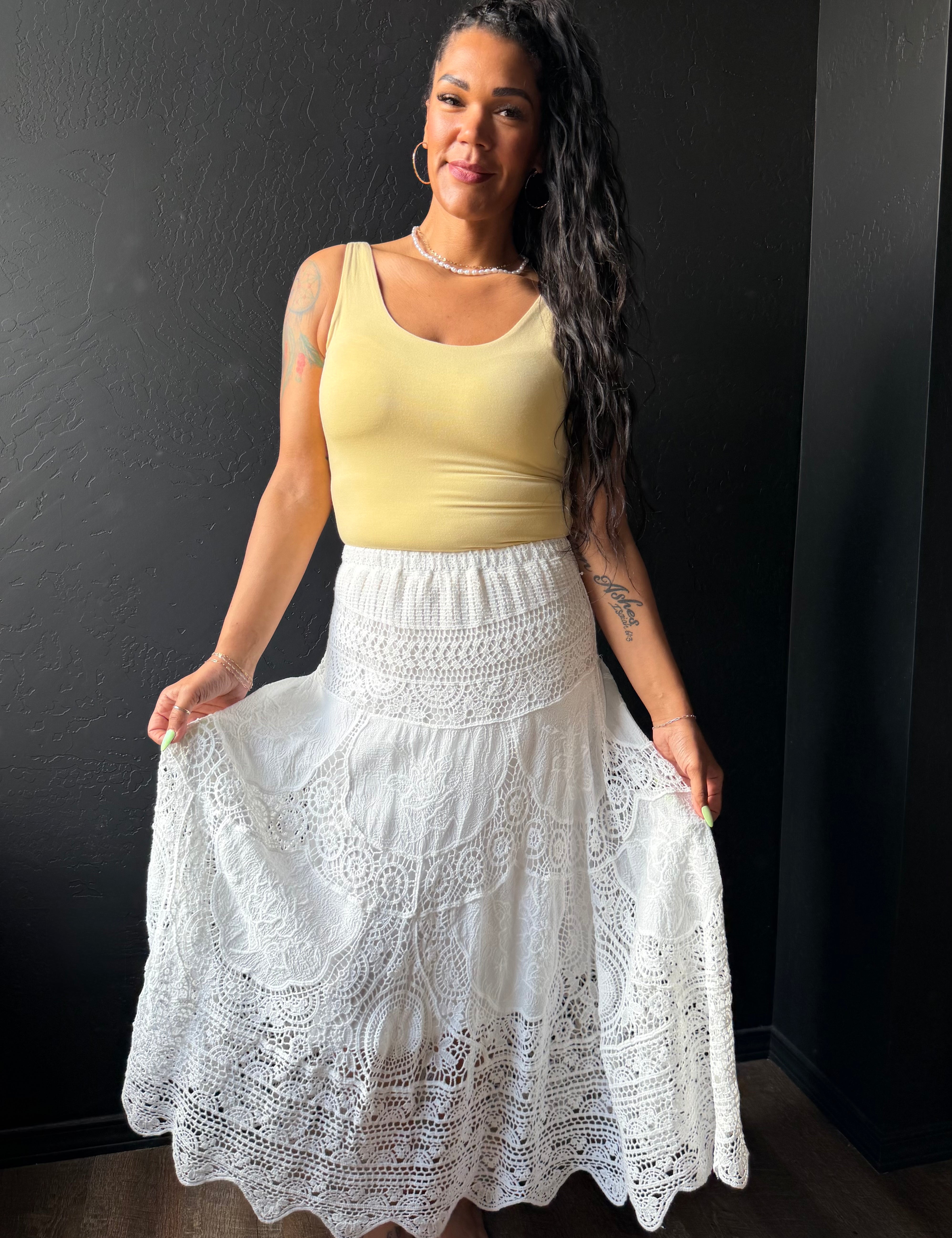 Woman wearing a yellow top and white lace skirt against a black background