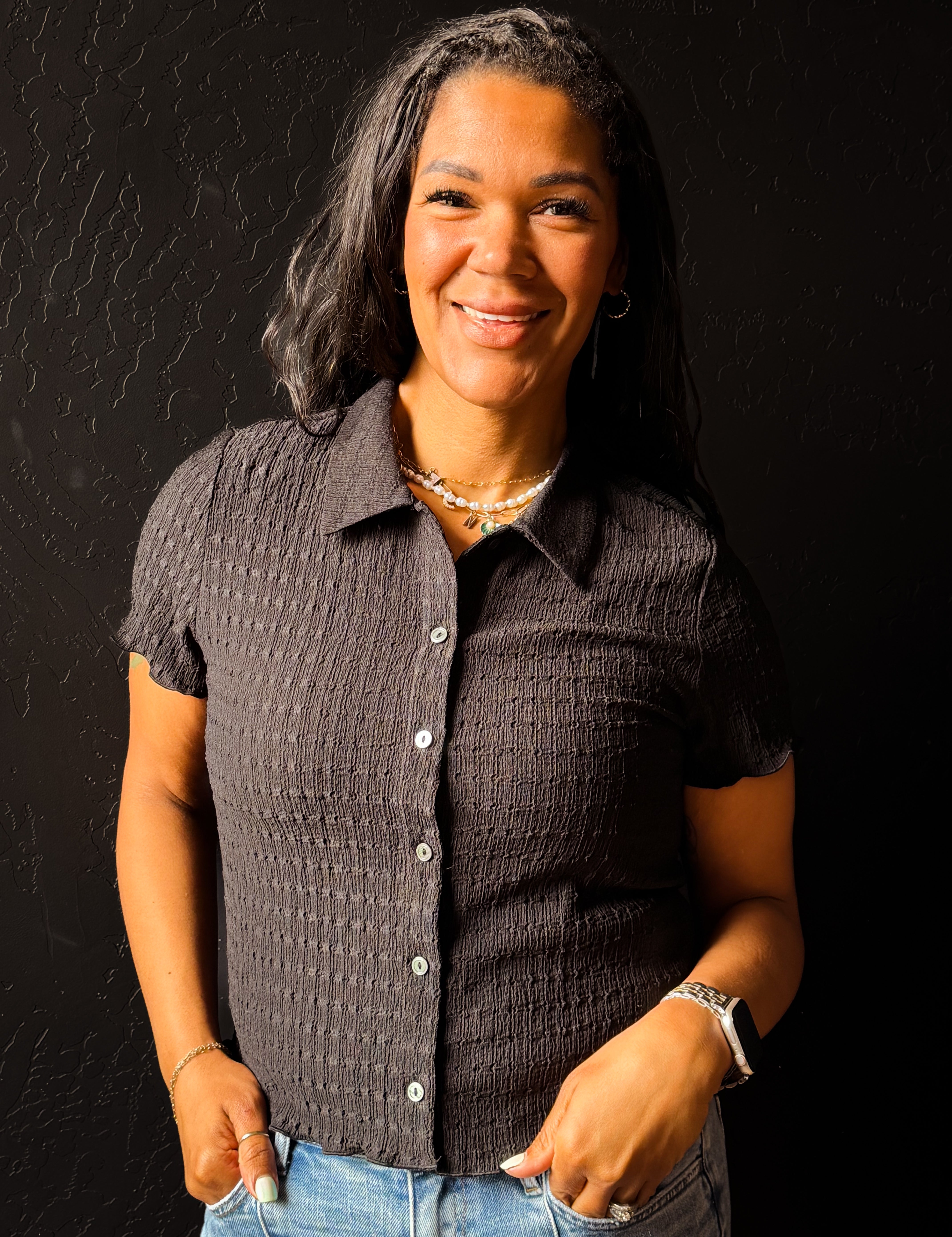 Woman wearing a textured dark shirt and jeans against a black background