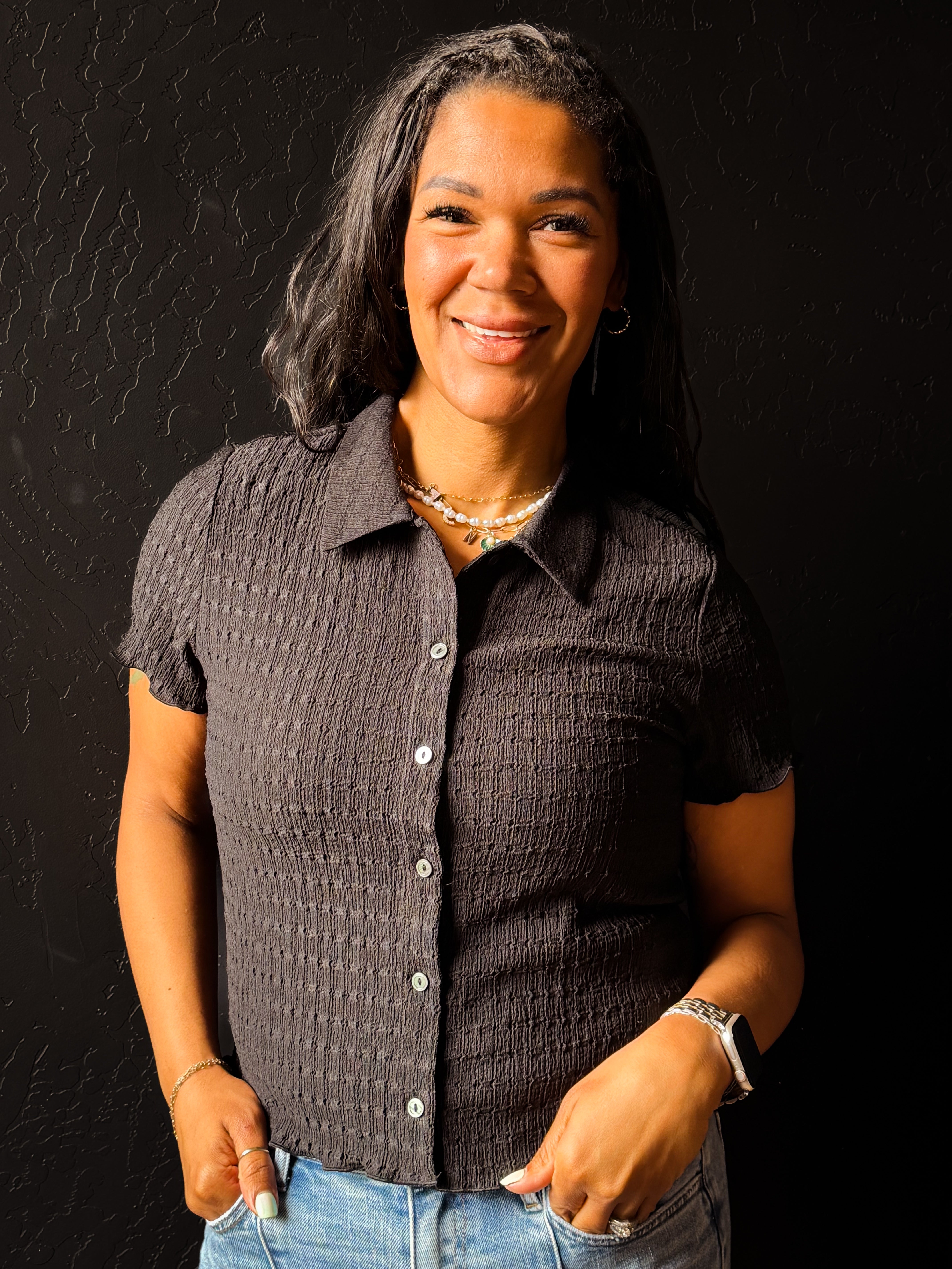 Woman wearing a textured dark shirt and jeans against a black background