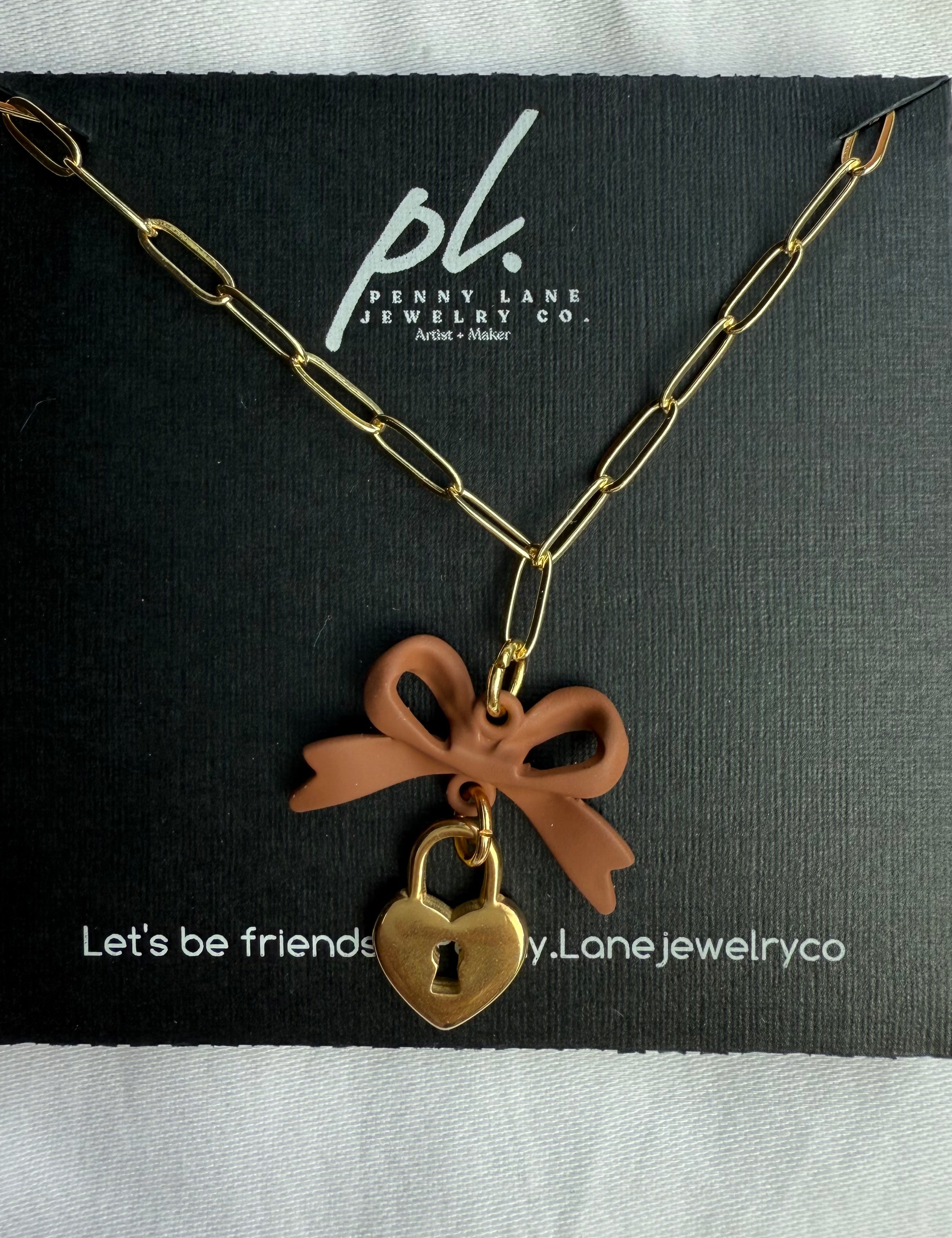 Necklace with a heart-shaped padlock and brown bow on a Penny Lane Jewelry Co. card.