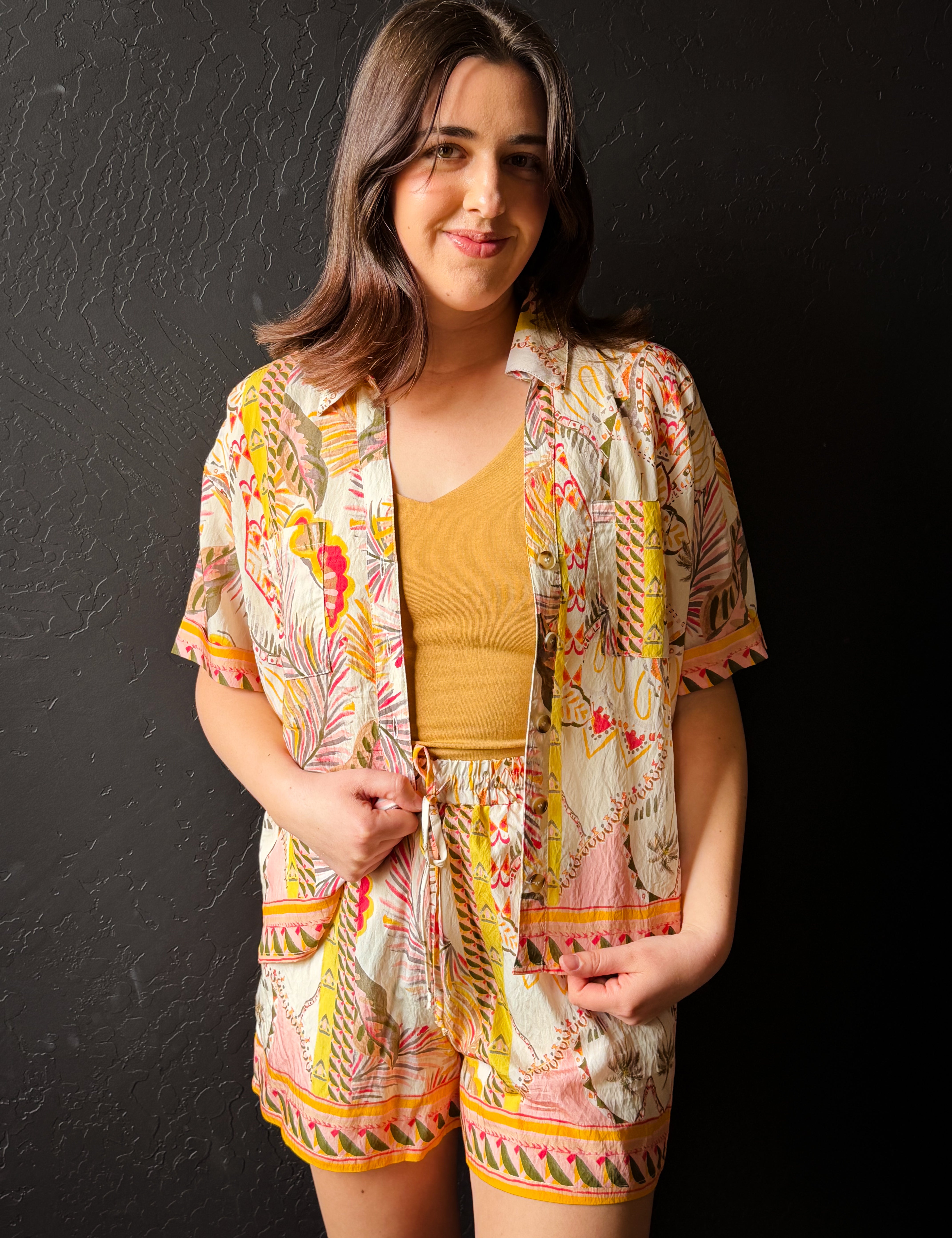 Woman wearing a colorful outfit with a patterned jacket and shorts against a black background