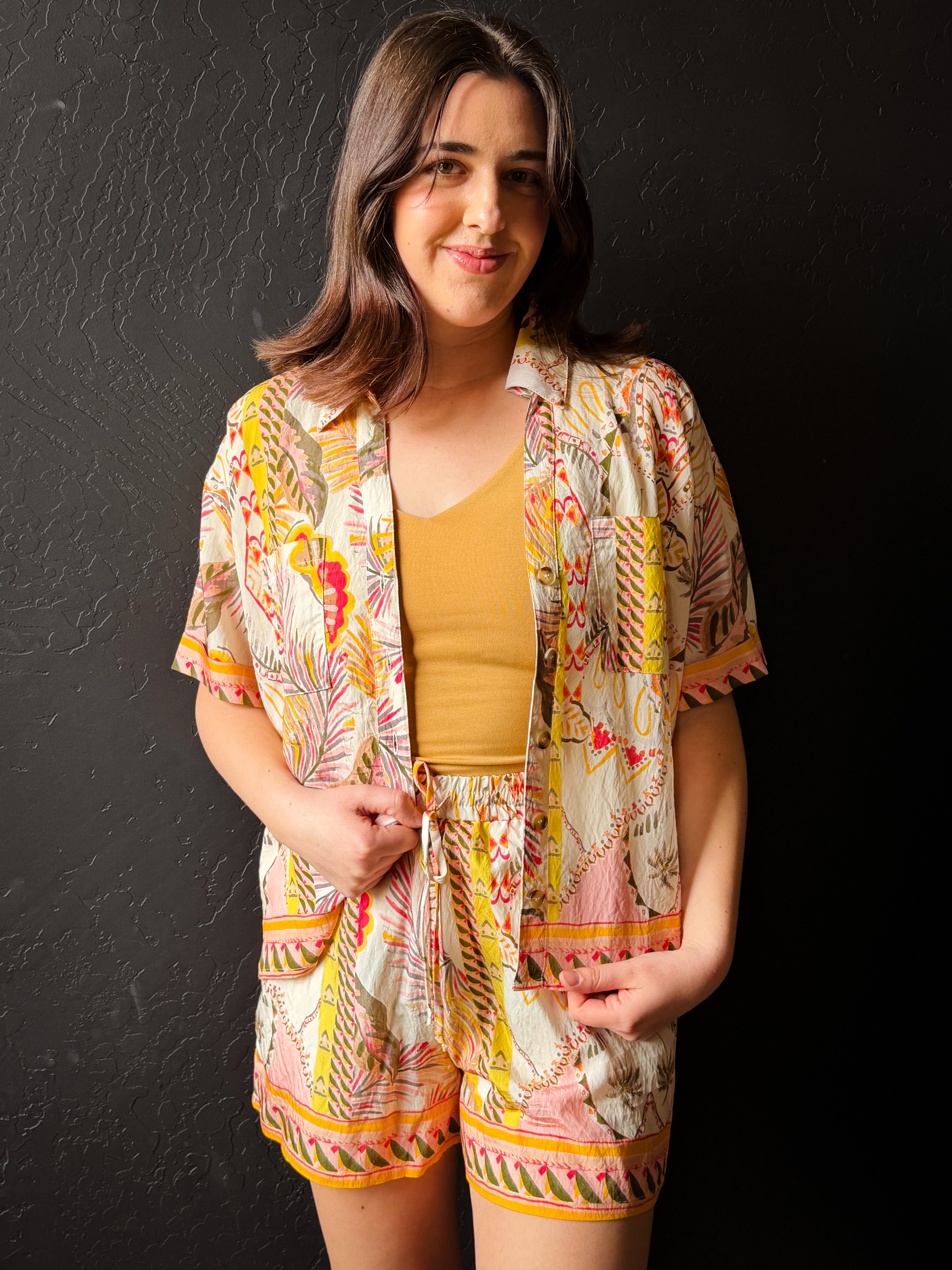 Woman wearing a colorful outfit with a patterned jacket and shorts against a black background