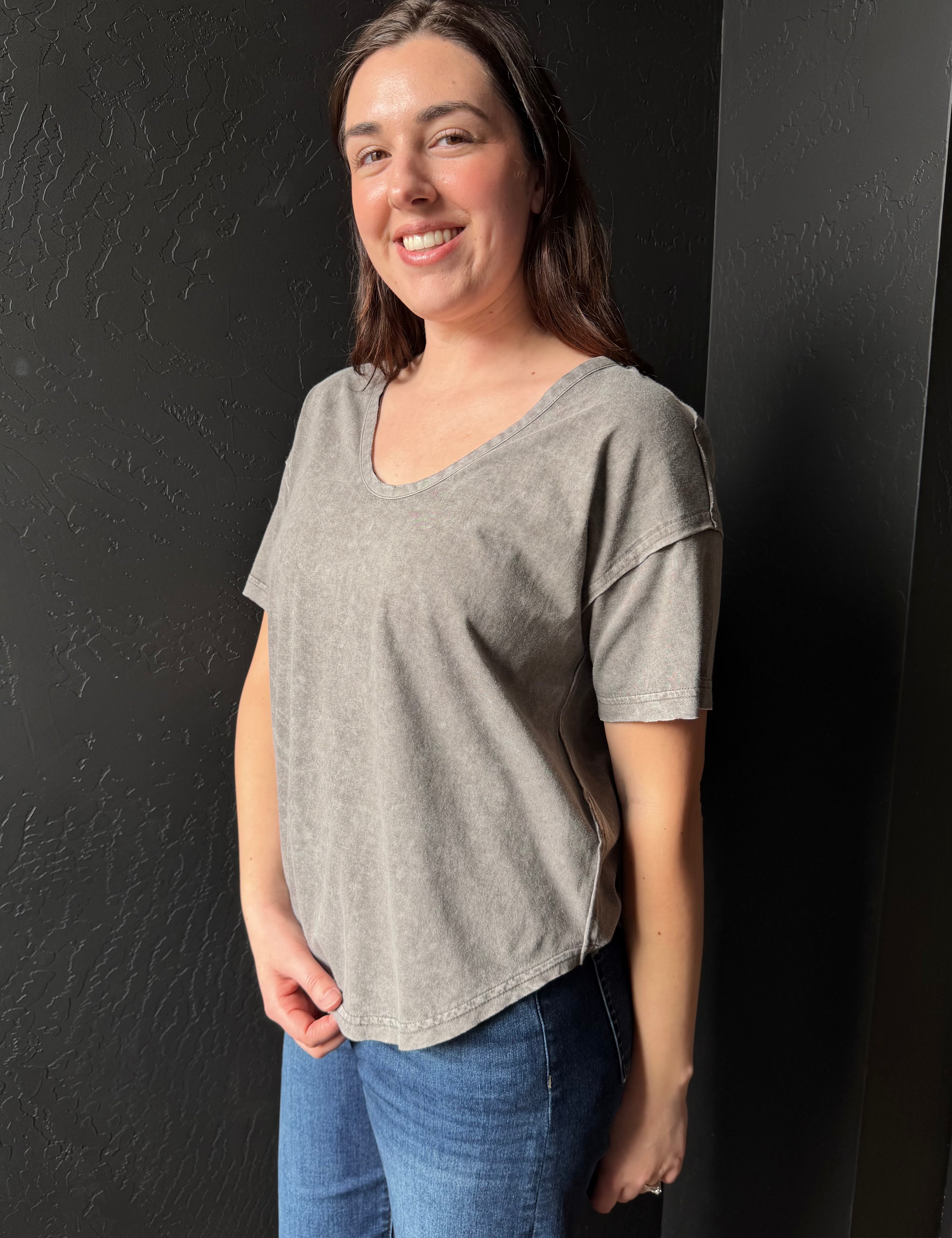 Woman wearing a gray t-shirt and blue jeans against a black background