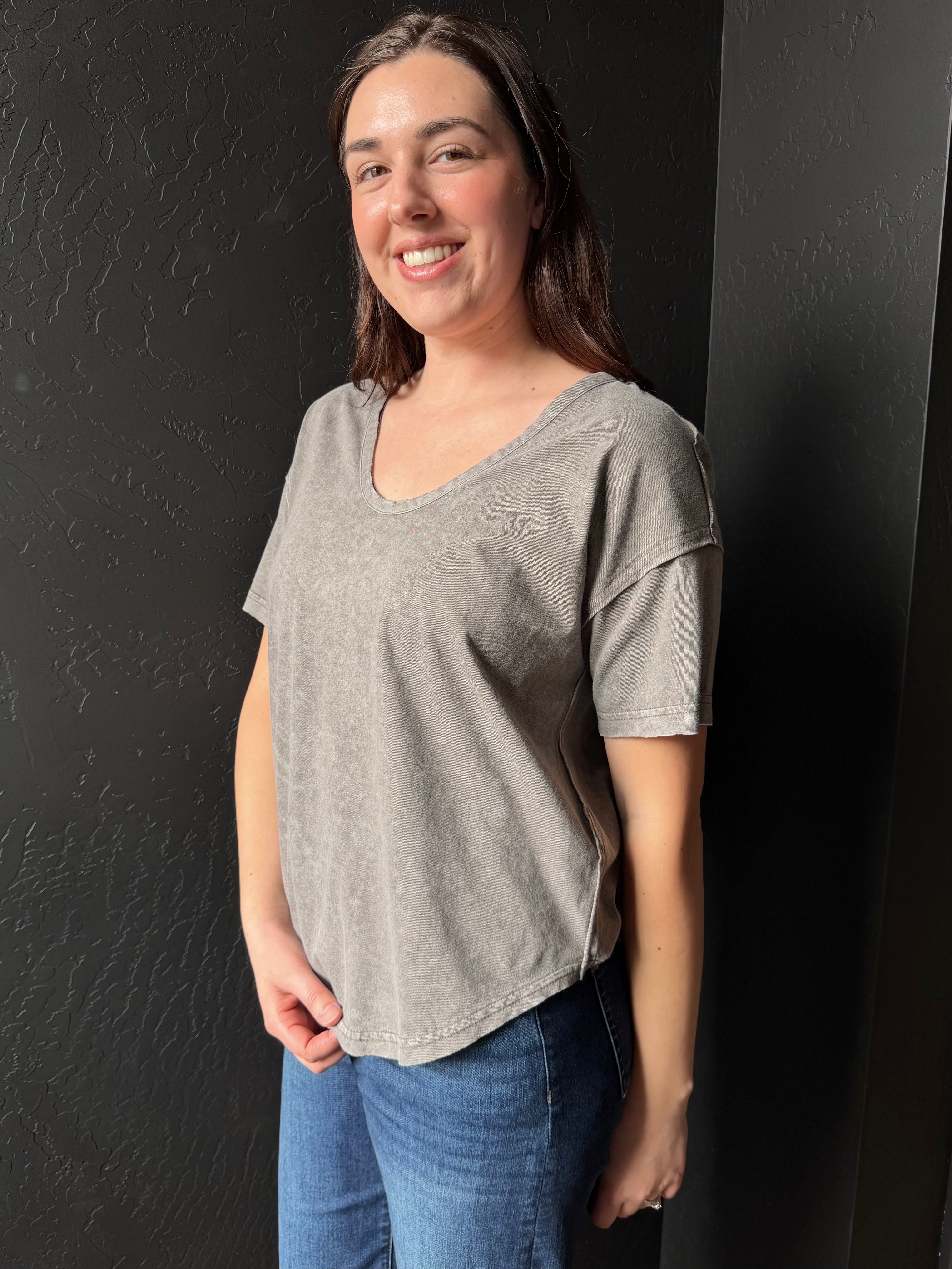 Woman wearing a gray t-shirt and blue jeans against a black background