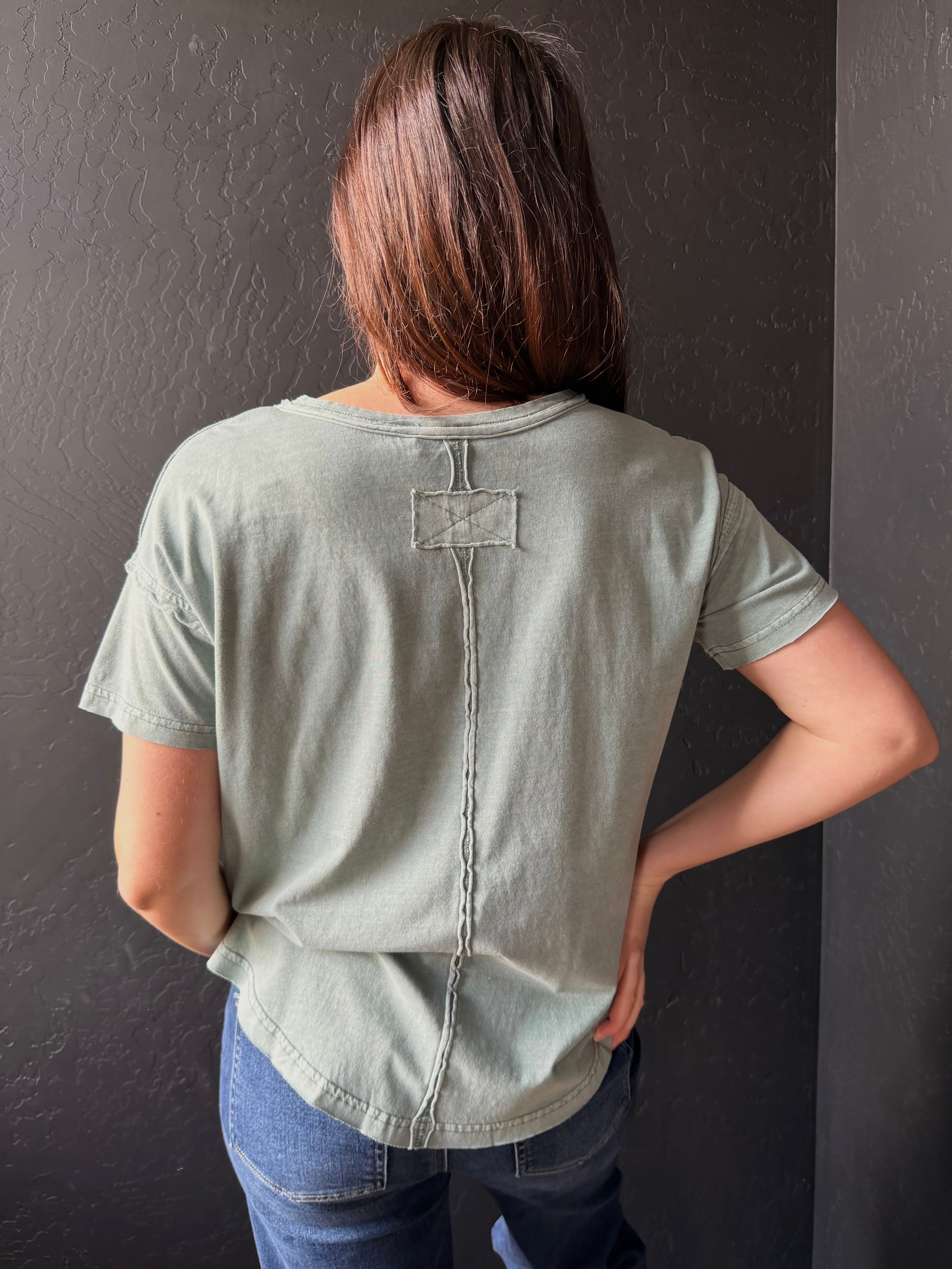 Person wearing a light green t-shirt with a button detail on a dark background
