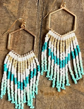 Beaded earrings with blue and white fringes on a wooden surface