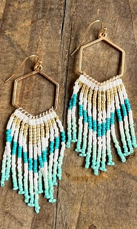 Beaded earrings with blue and white fringes on a wooden surface