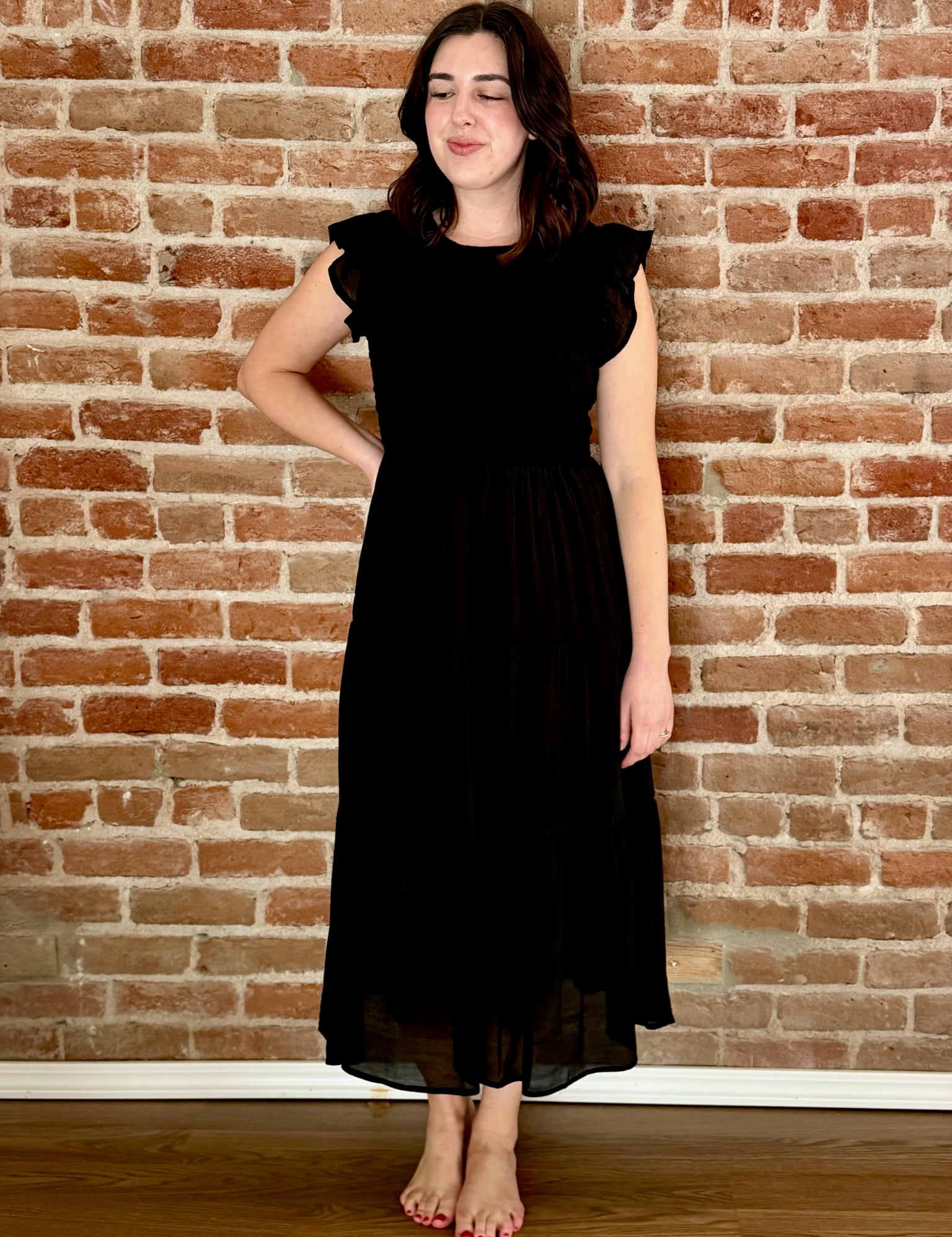 Woman wearing a black dress standing against a brick wall.