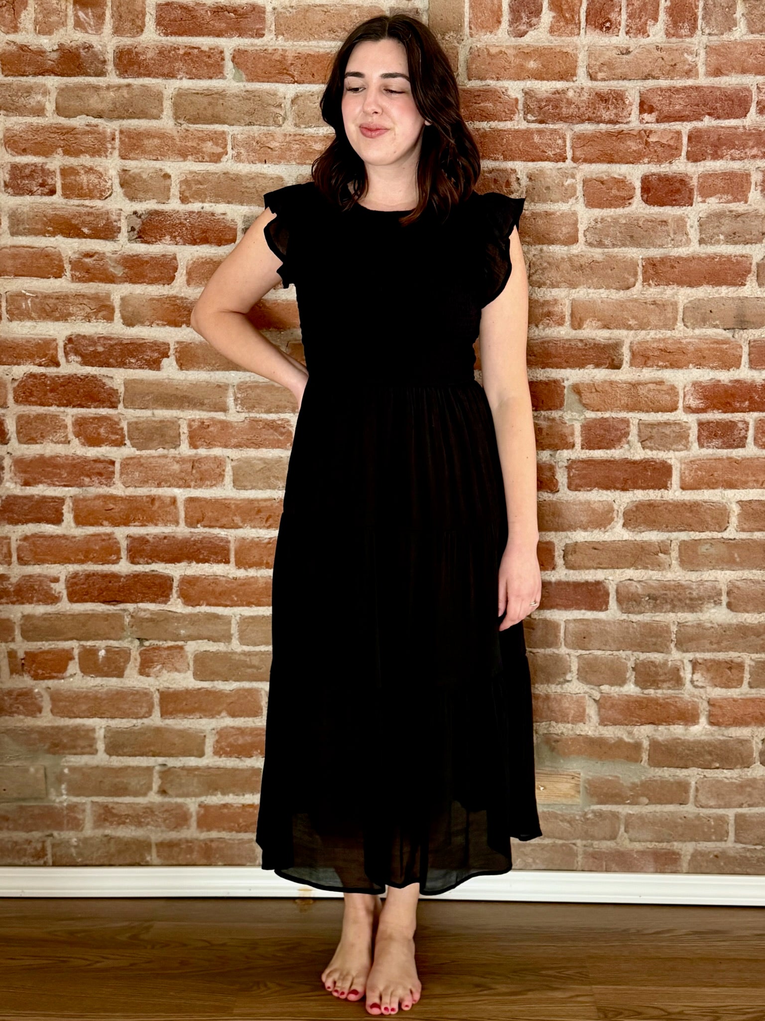 Woman wearing a black dress standing against a brick wall.