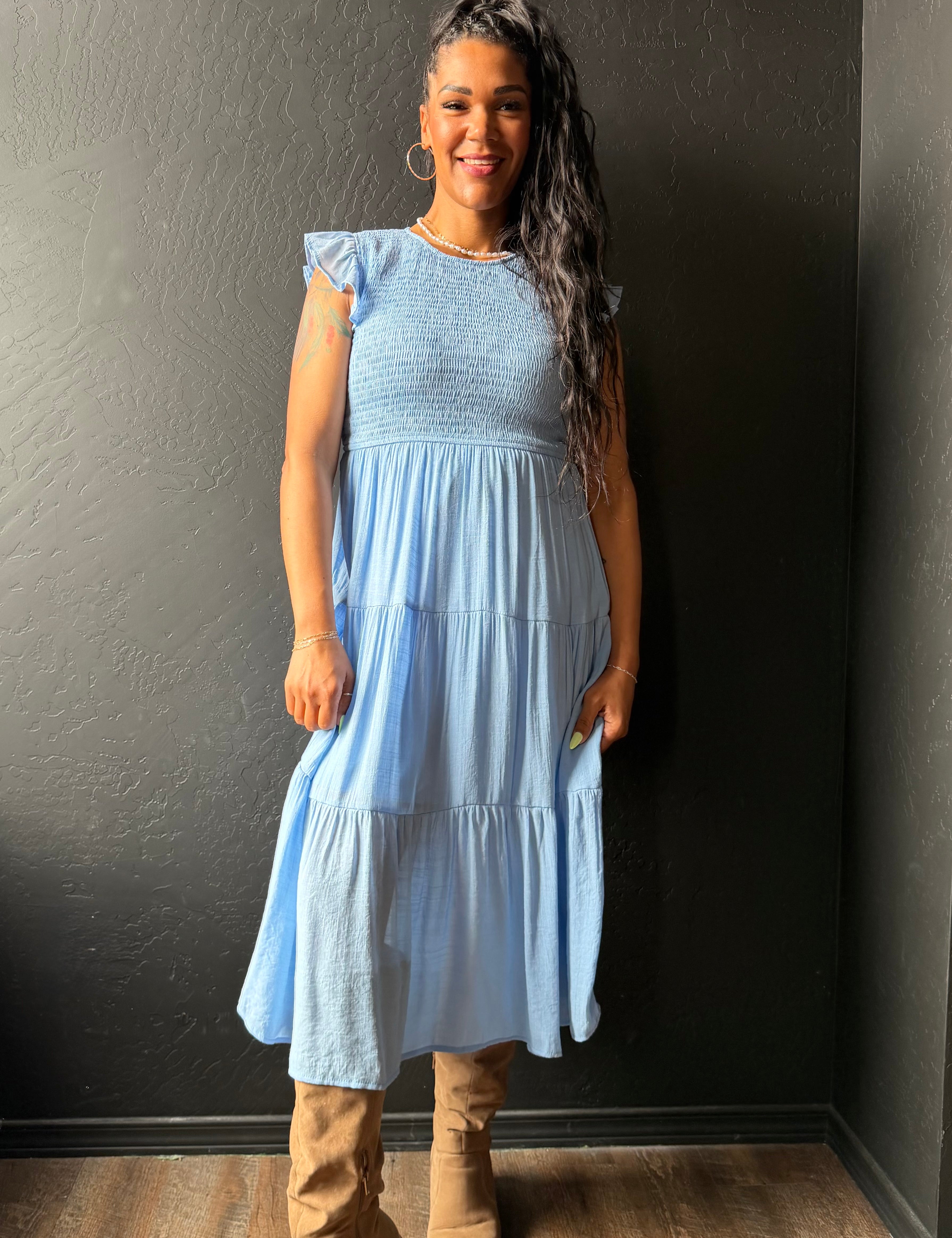 Woman wearing a light blue dress standing against a dark wall.