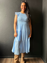 Woman wearing a light blue dress standing against a dark wall.