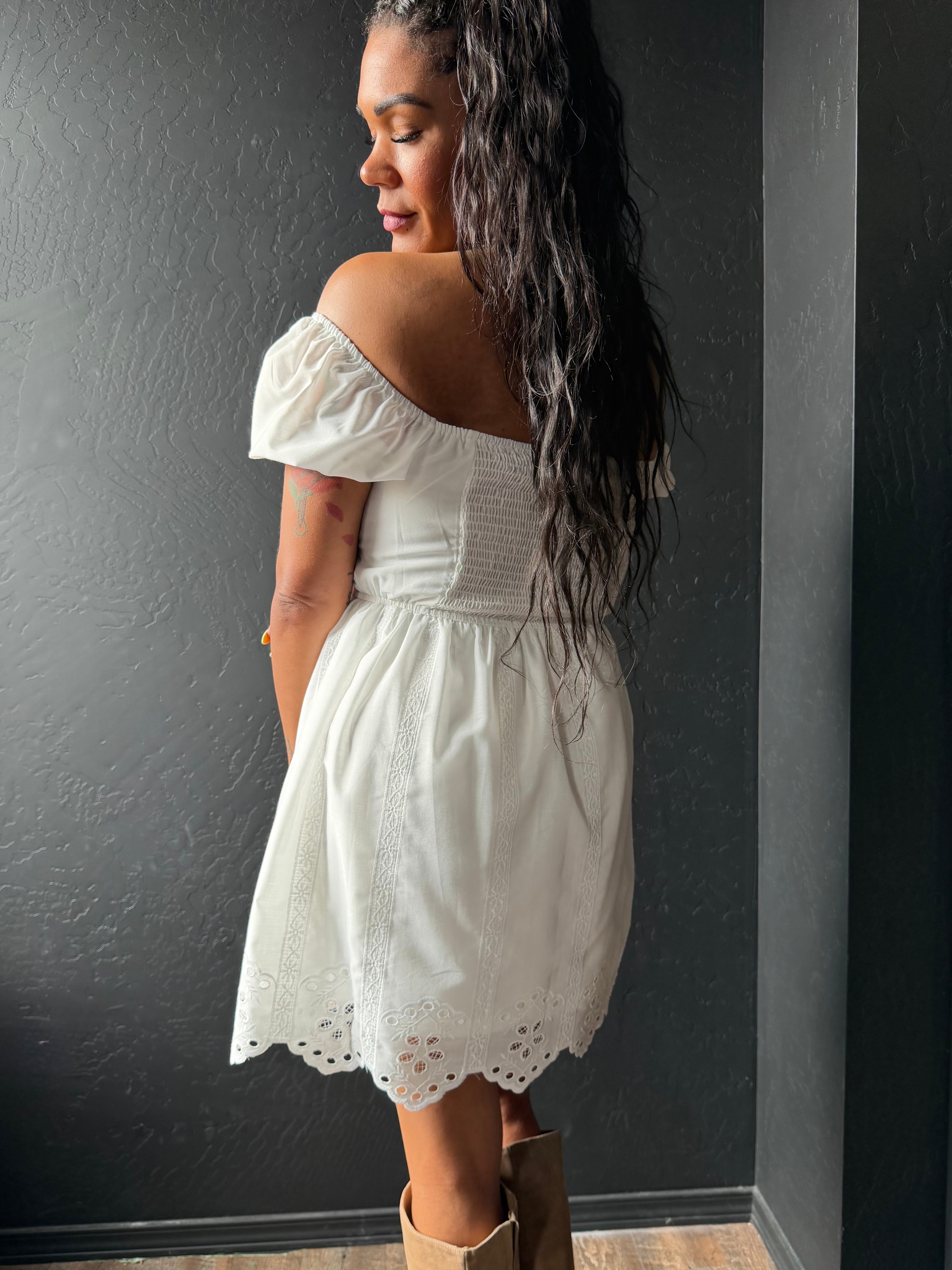 Woman wearing a white off-shoulder dress against a dark wall.
