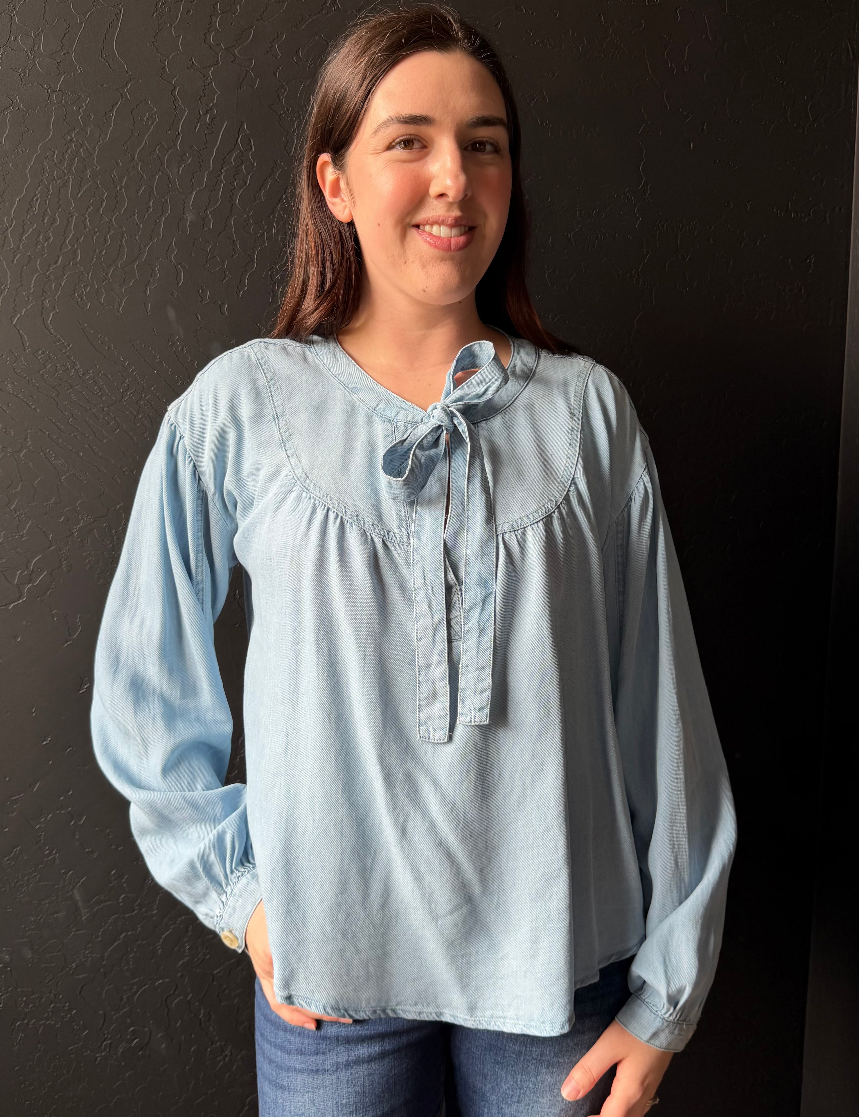 Woman wearing a light blue blouse with a dark background