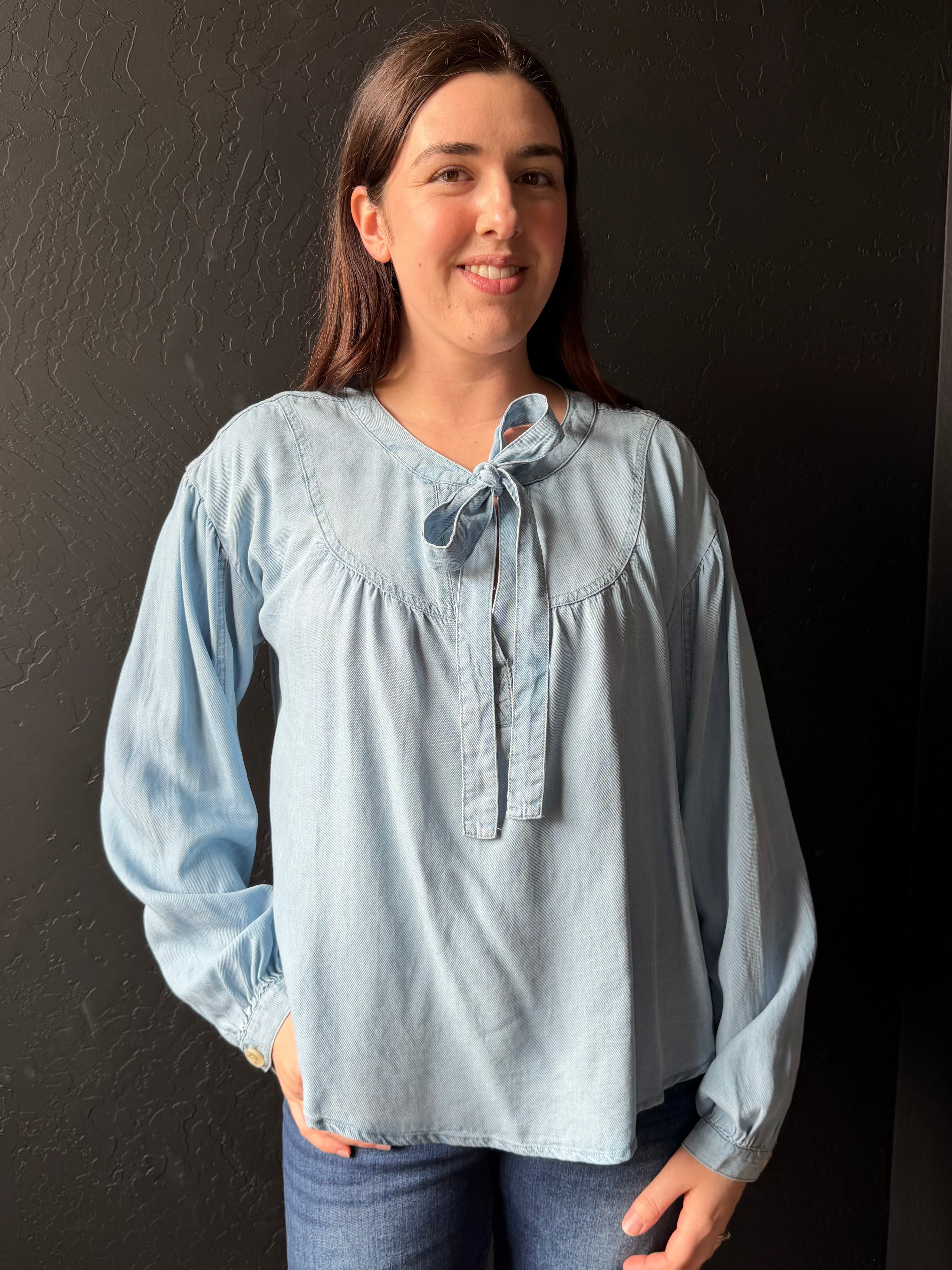 Woman wearing a light blue blouse with a dark background