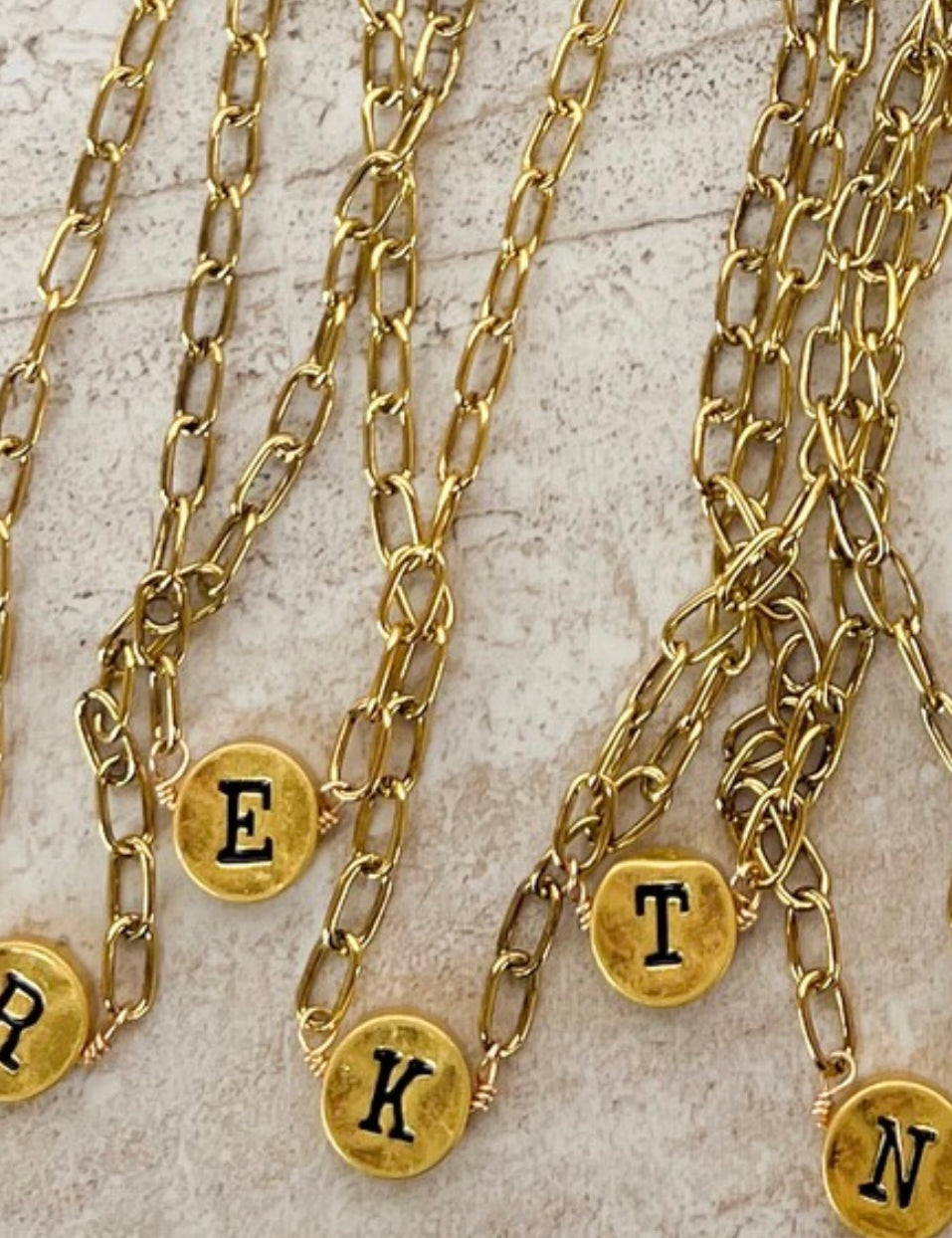 Gold chain necklaces with lettered pendants on a textured surface