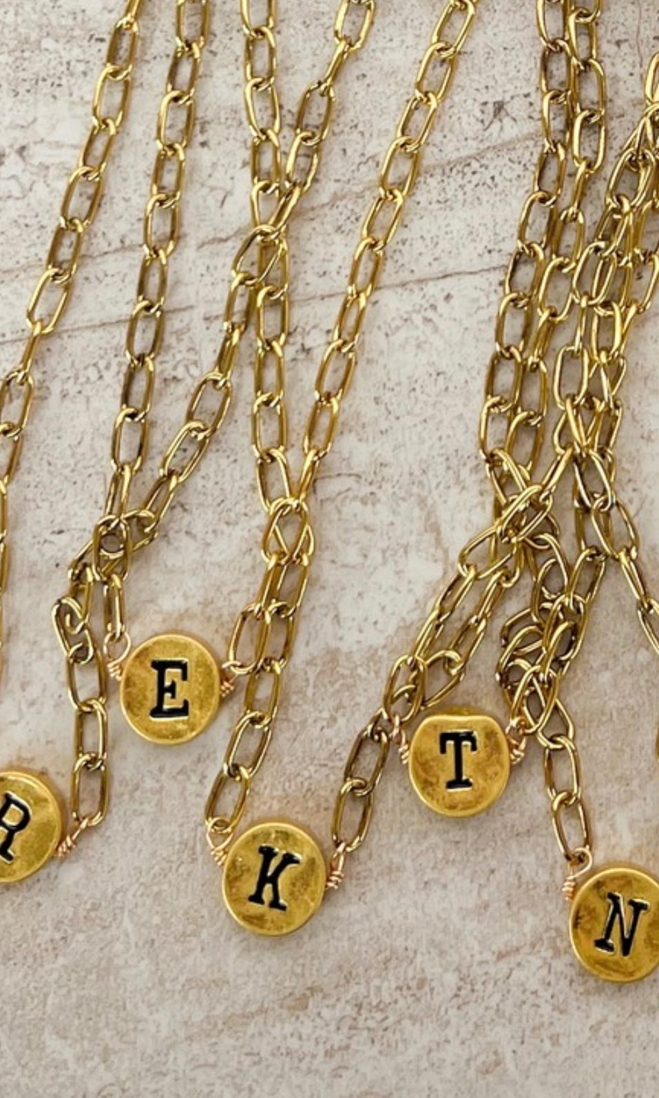 Gold chain necklaces with lettered pendants on a textured surface