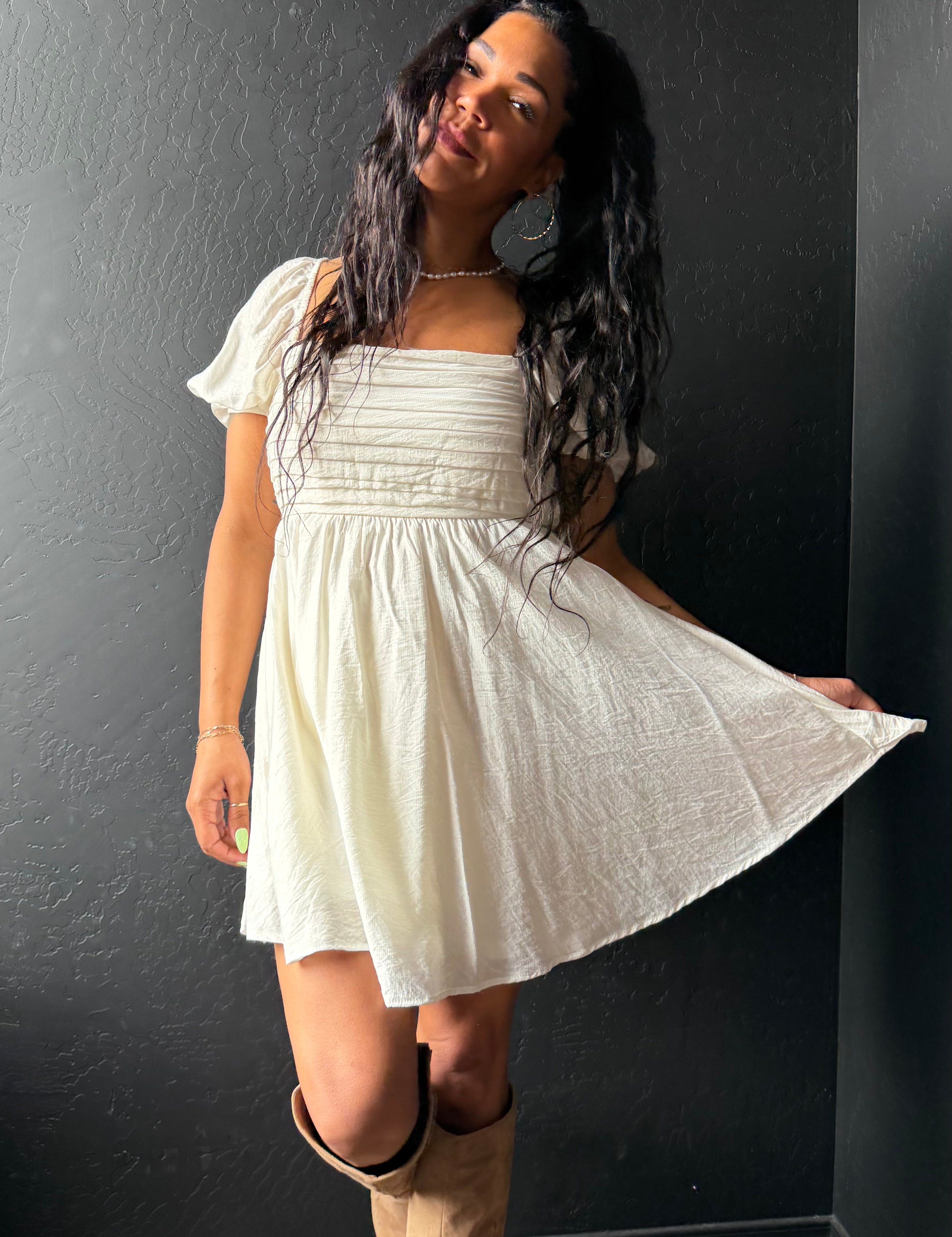 Woman wearing a white dress with puffed sleeves against a dark wall.