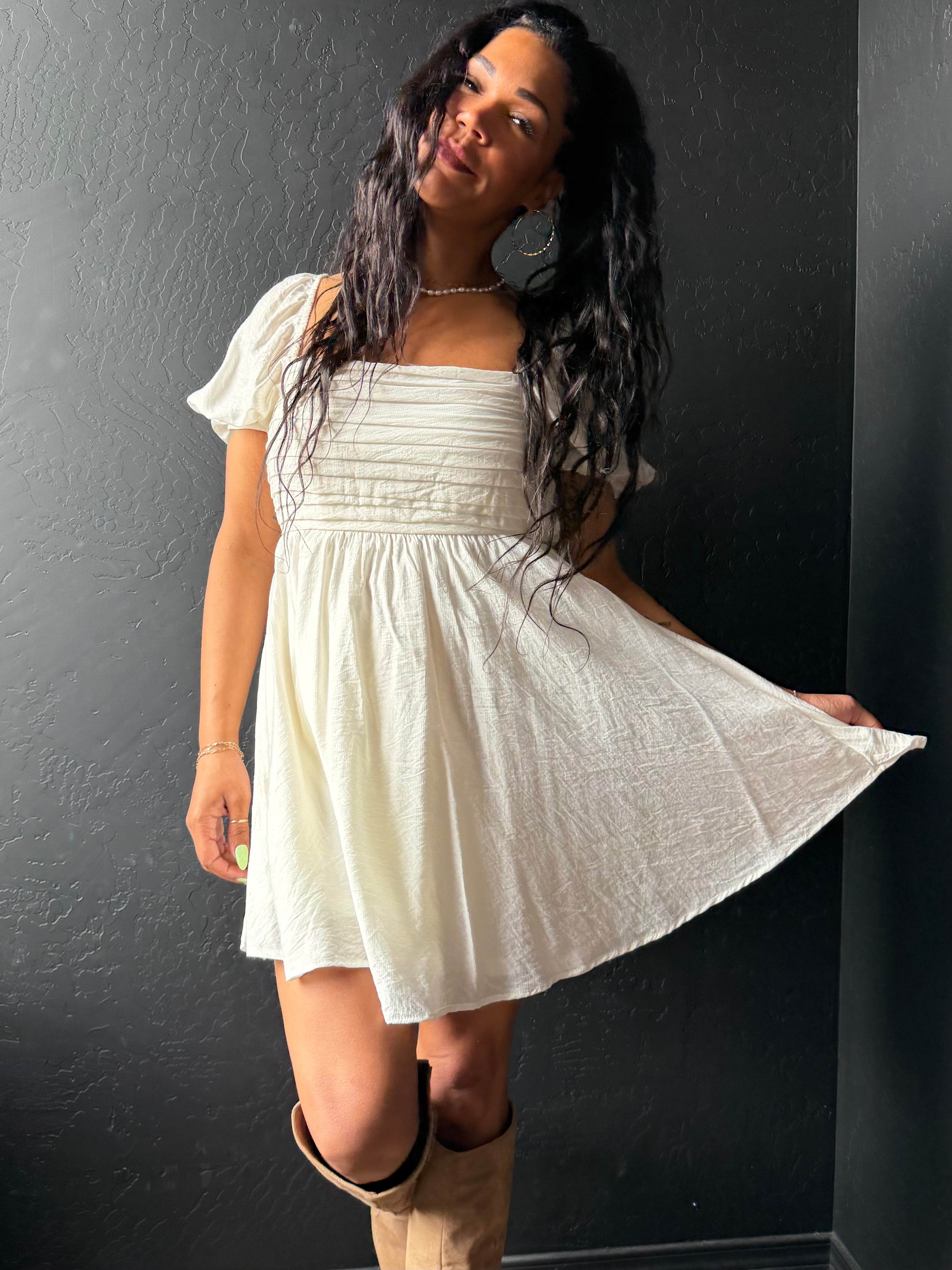 Woman wearing a white dress with puffed sleeves against a dark wall.