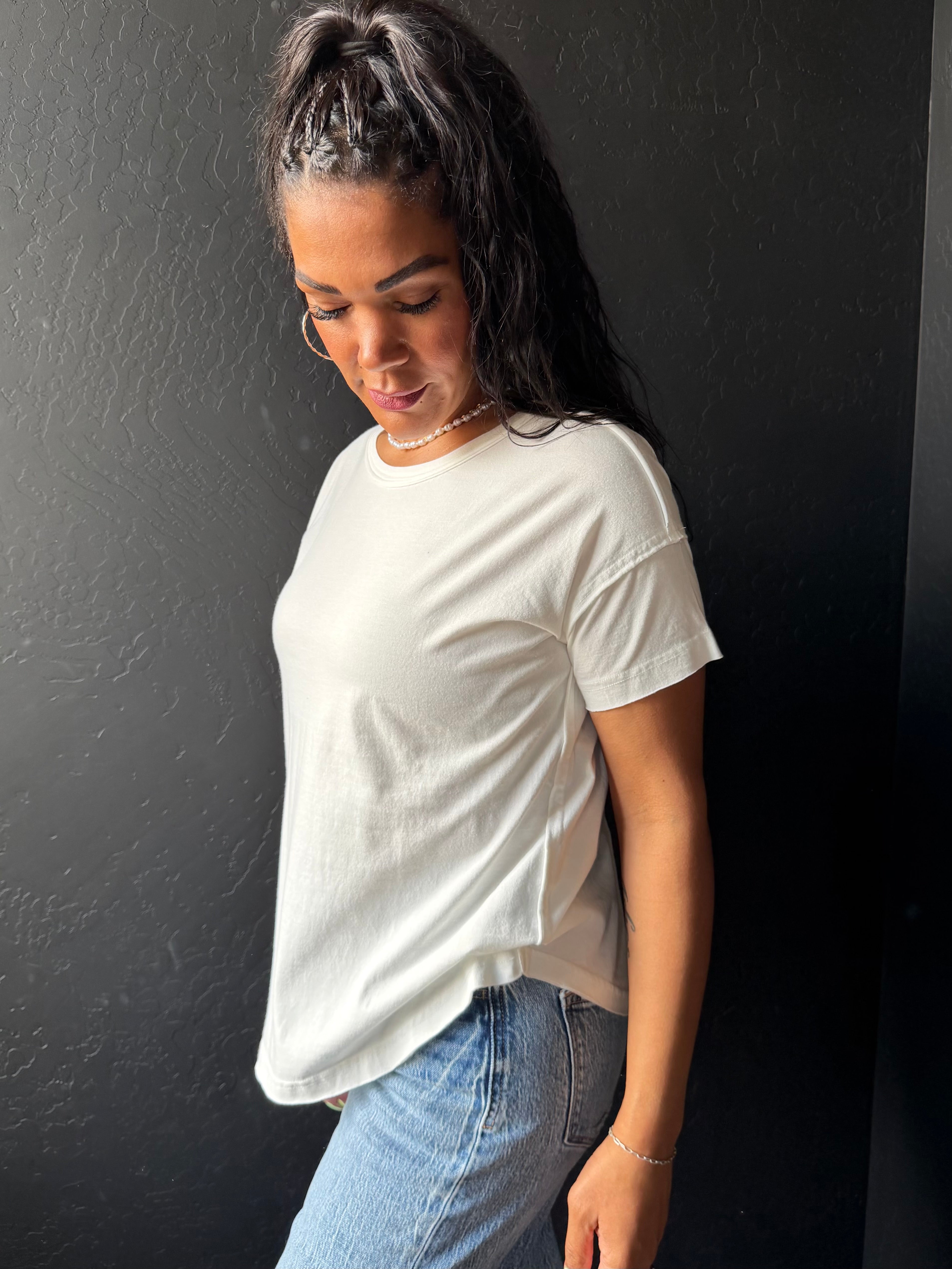 Woman wearing a white t-shirt and blue jeans against a black wall