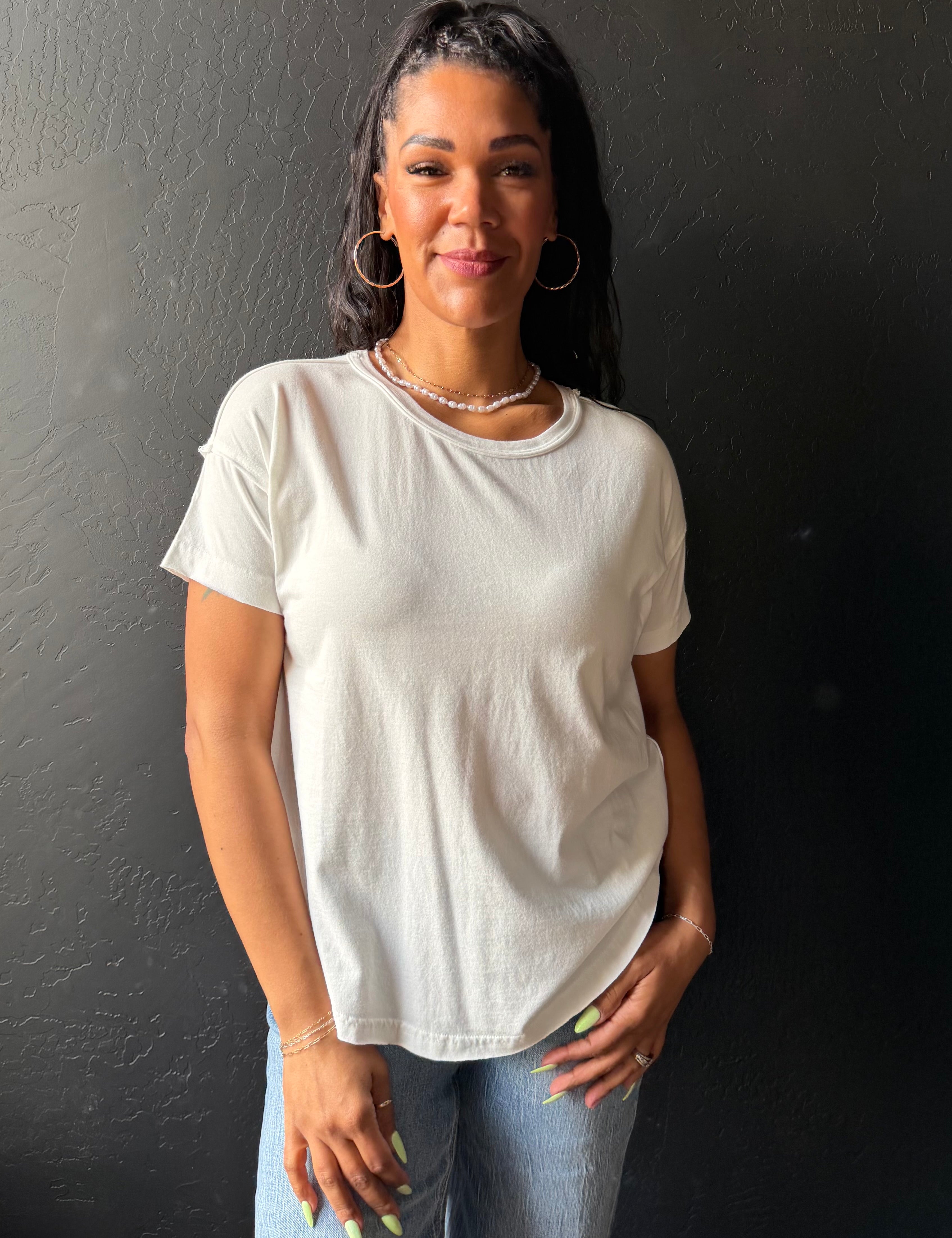 Woman wearing a white t-shirt and jeans against a dark background