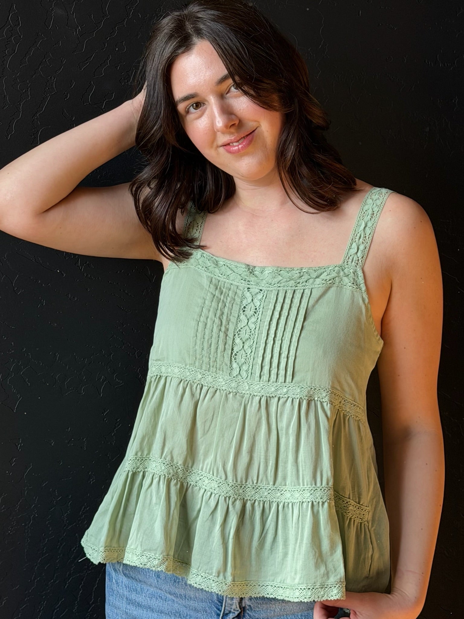 Woman wearing a light green sleeveless top against a black background