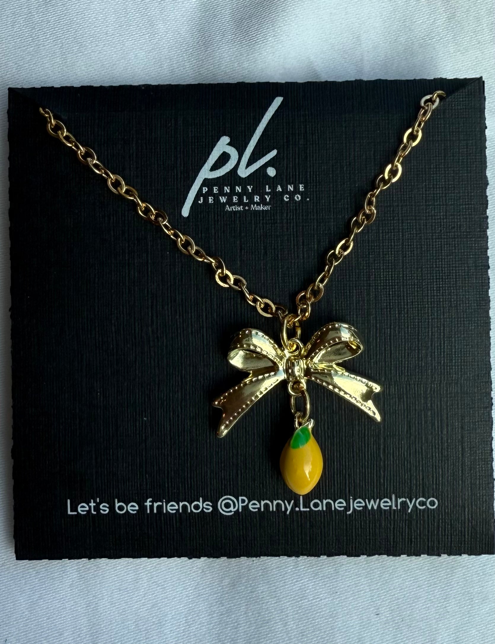 Gold necklace with a bow and green pendant on a Penny Lane Jewelry card.