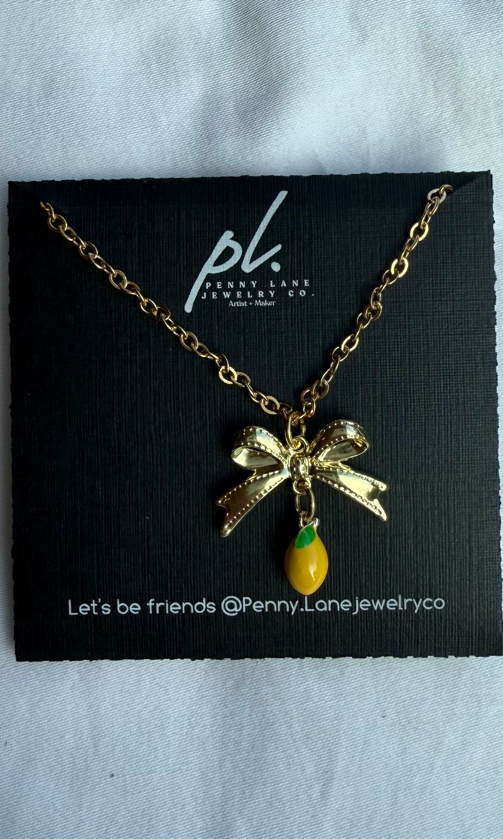 Gold necklace with a bow and green pendant on a Penny Lane Jewelry card.
