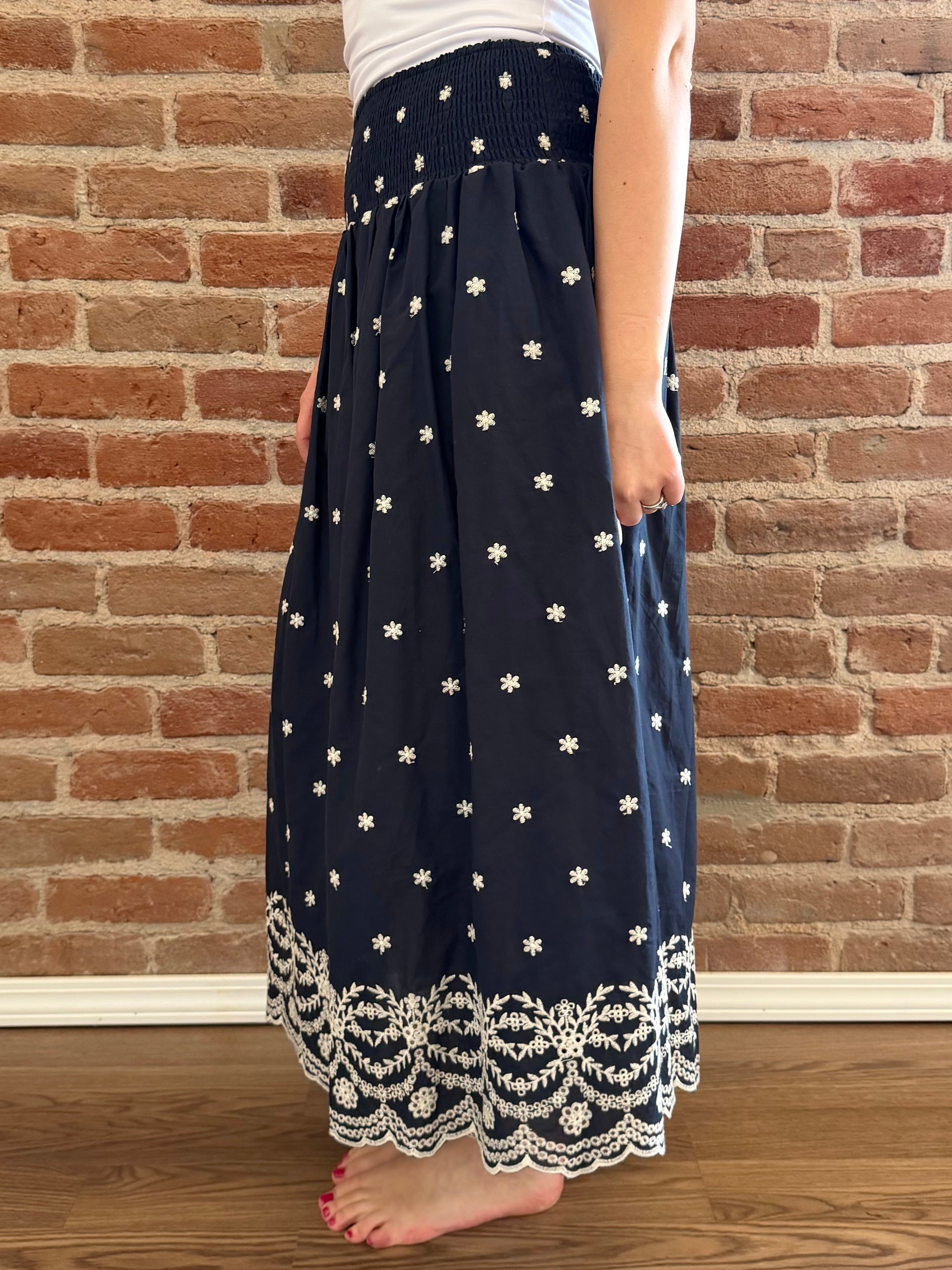 Navy blue skirt with white floral pattern and lace trim worn by a person against a brick wall.
