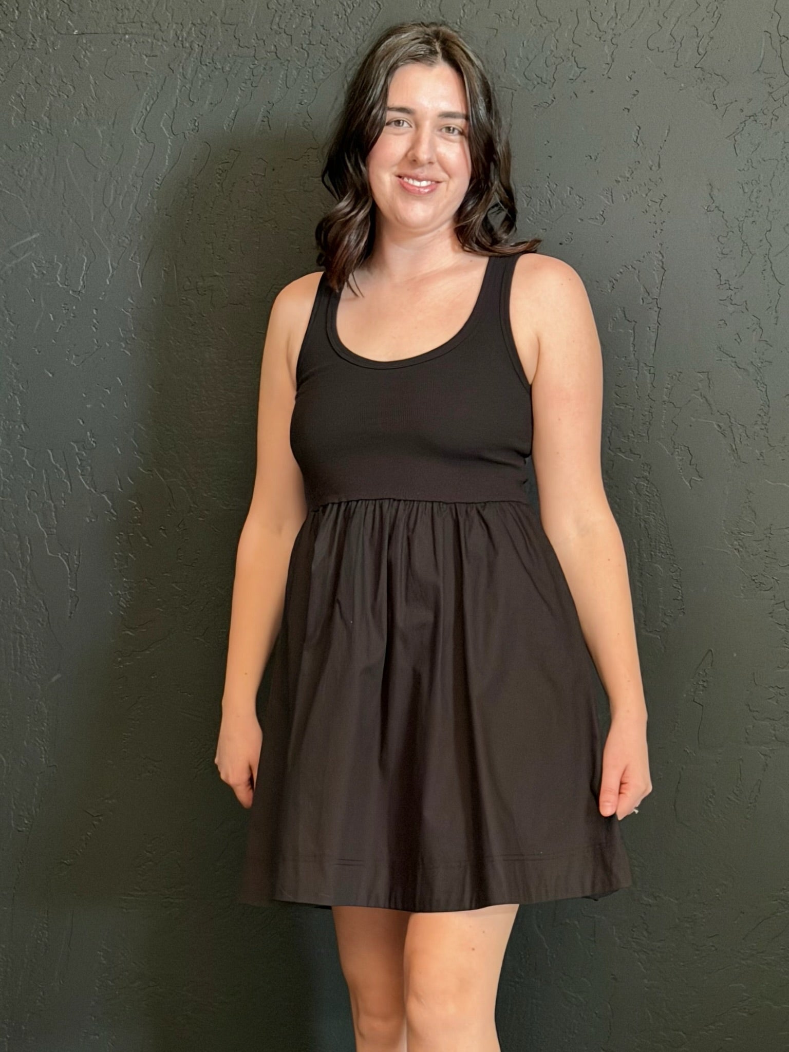 Woman wearing a black sleeveless dress against a dark wall