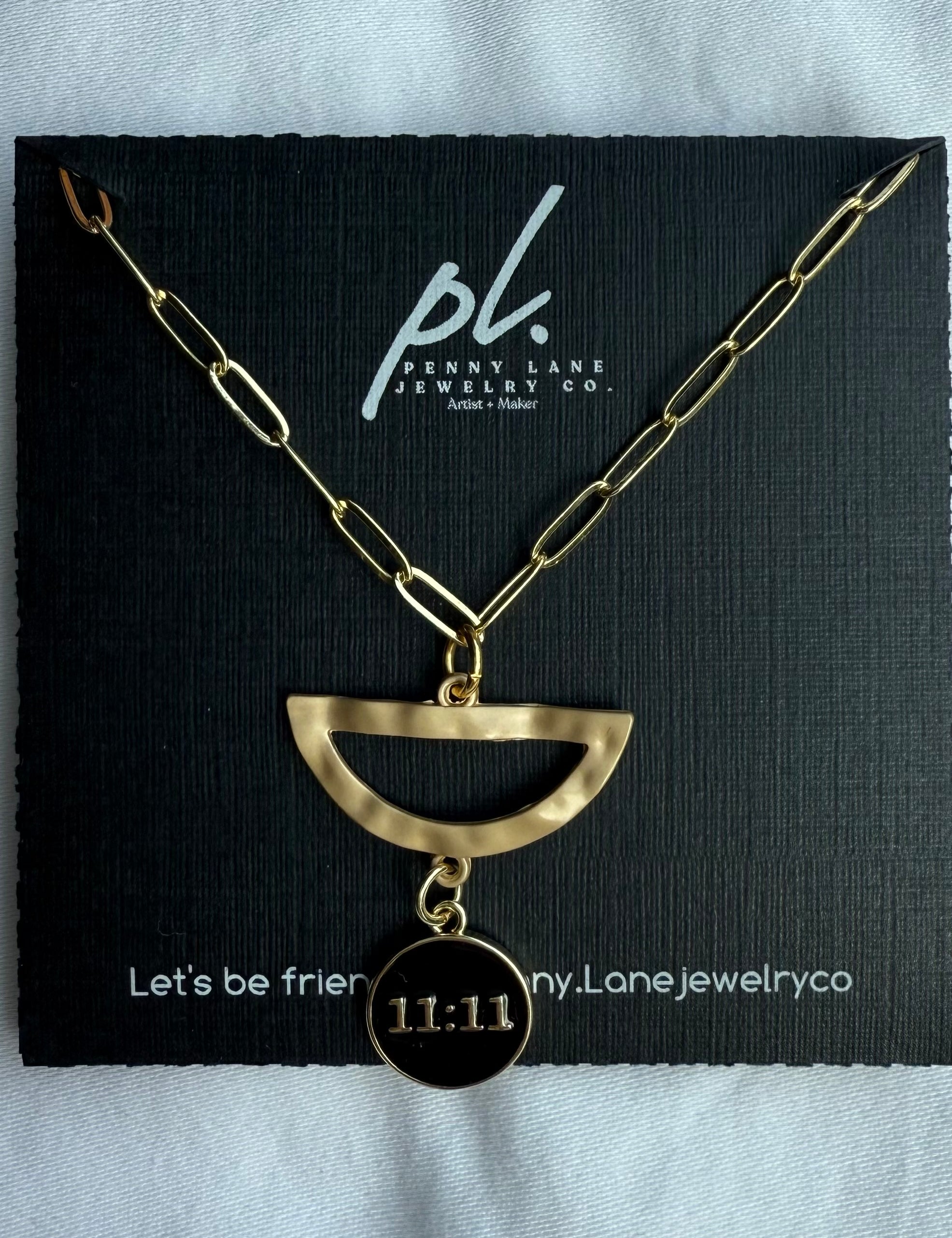 Gold necklace with a half-circle pendant and '11:11' charm on a black card with 'penny lane jewelry co' branding.