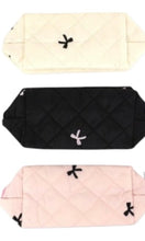 Three quilted pouches in beige, black, and pink with decorative bows on a white background.