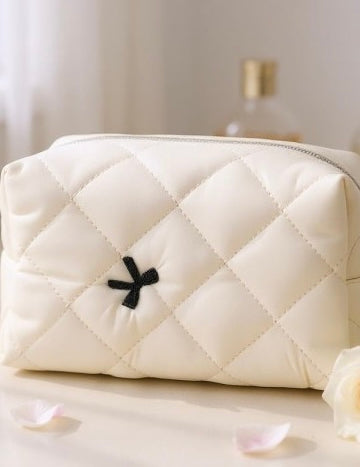 White quilted handbag with a black flower detail on a light surface.