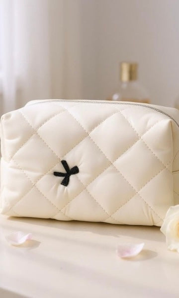 White quilted handbag with a black flower detail on a light surface.
