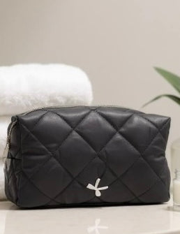 Black quilted cosmetic bag with a brand logo on a light surface.