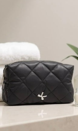 Black quilted cosmetic bag with a brand logo on a light surface.