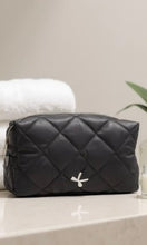 Black quilted cosmetic bag with a brand logo on a light surface.