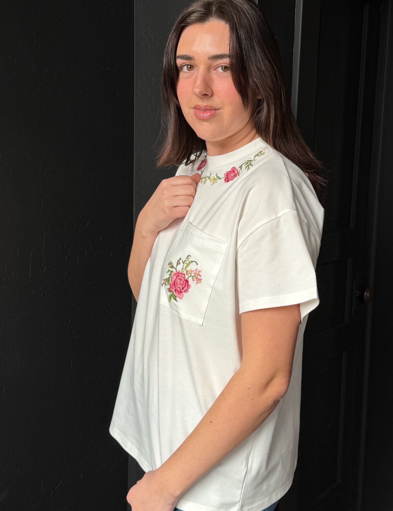Woman wearing a white t-shirt with floral embroidery against a black background