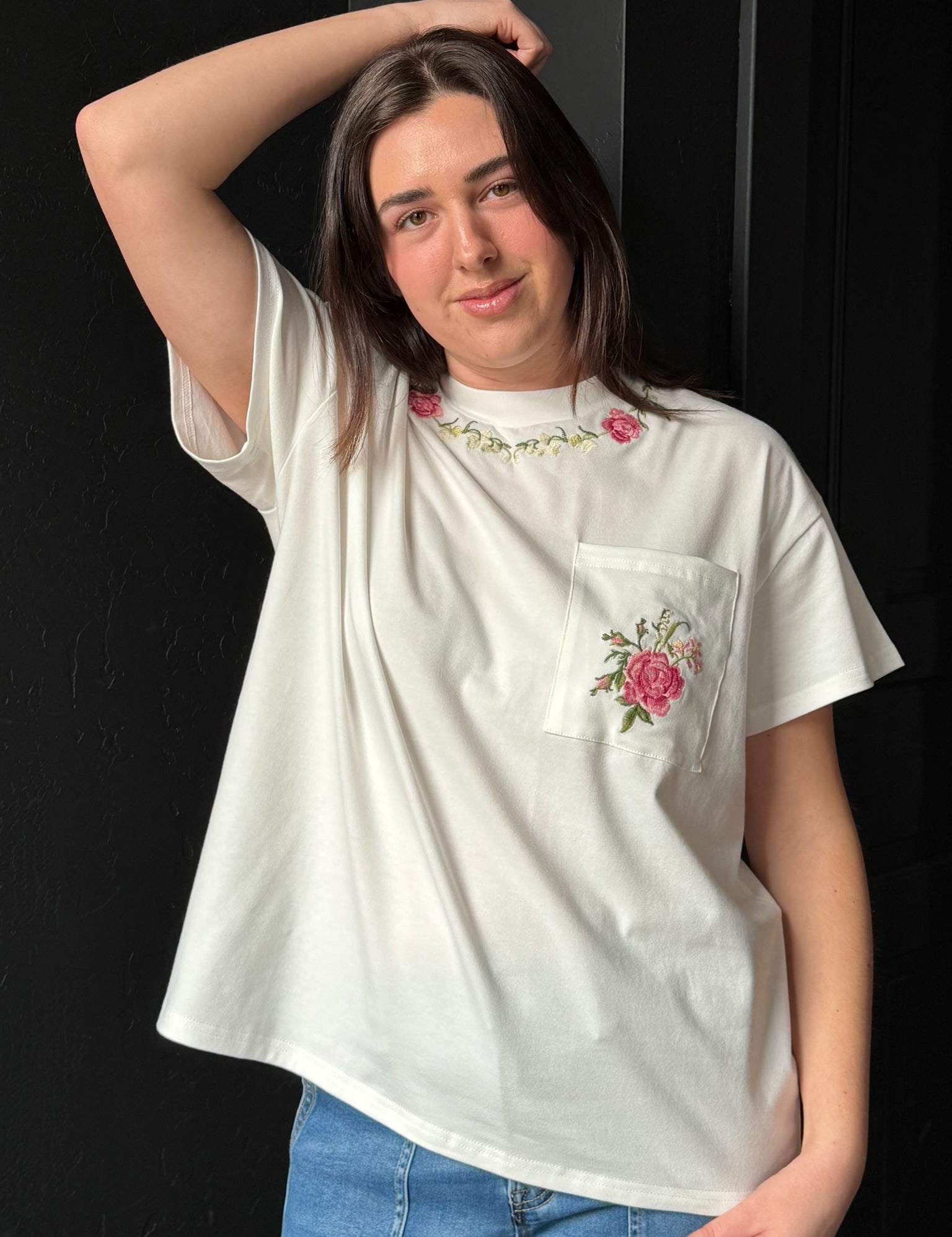 Person wearing a white t-shirt with floral embroidery on a black background