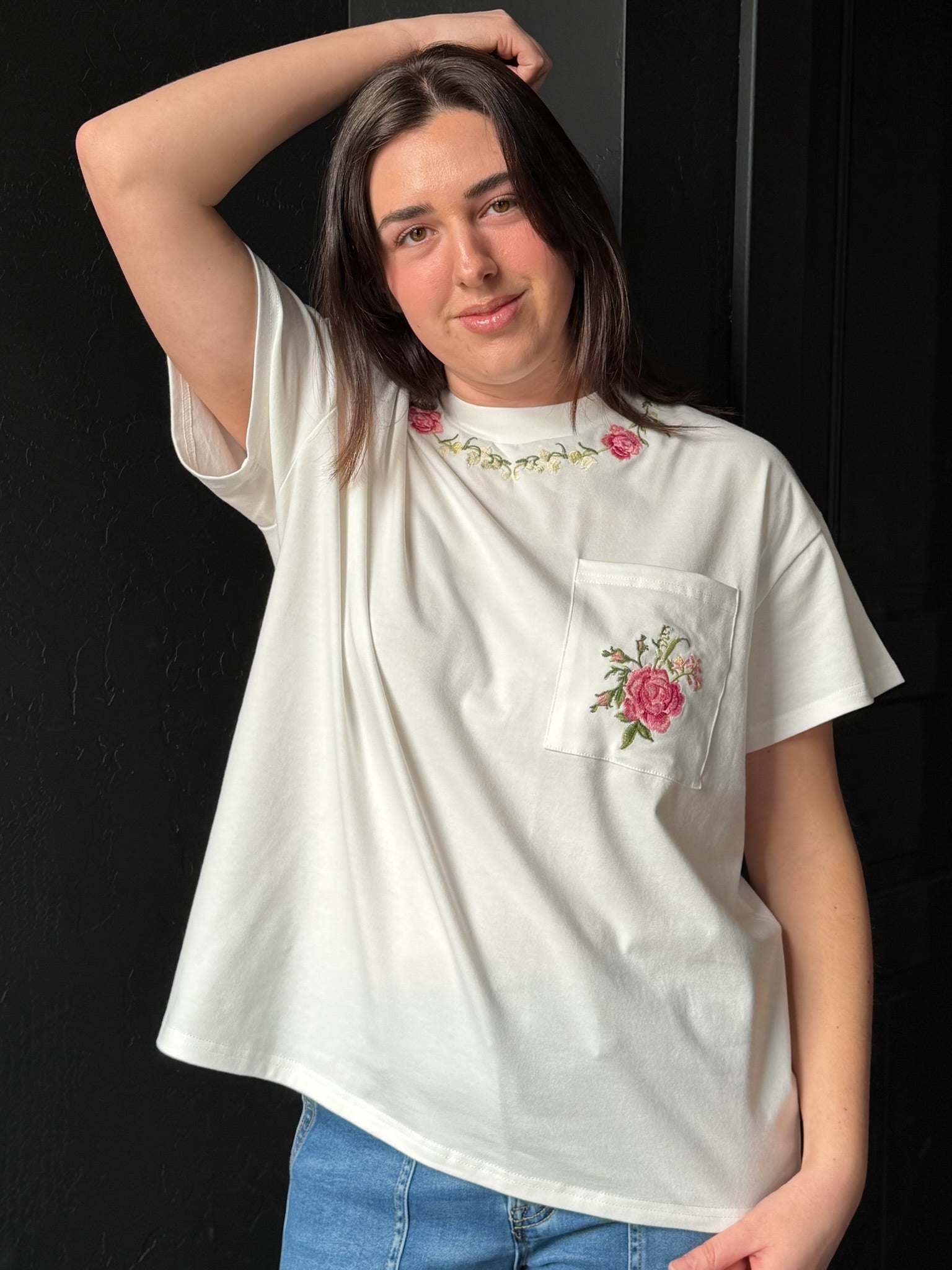 Person wearing a white t-shirt with floral embroidery on a black background