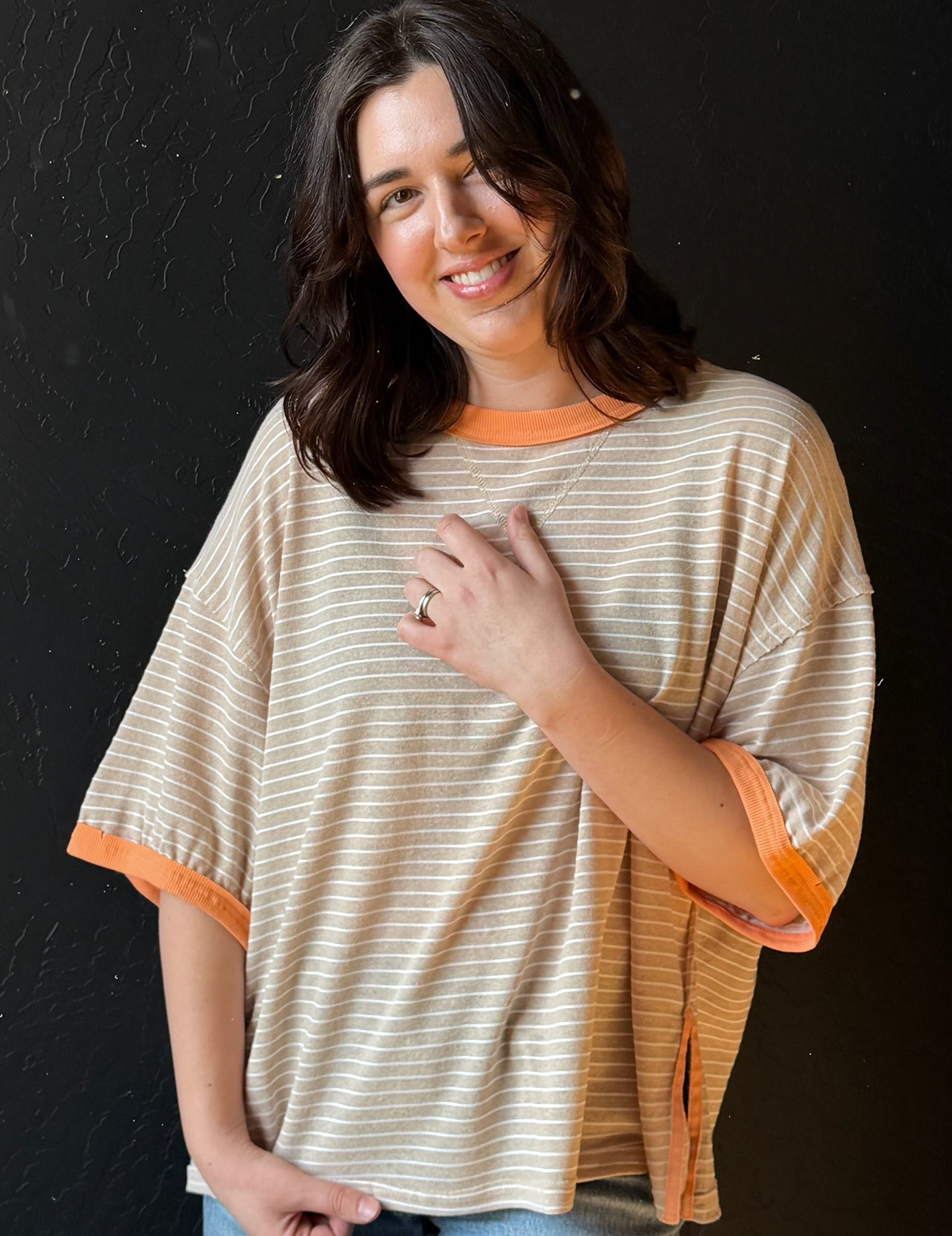 Woman wearing a beige and orange striped shirt against a black background