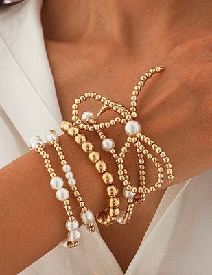 Gold and pearl beaded bracelets on a person's wrist with a white background
