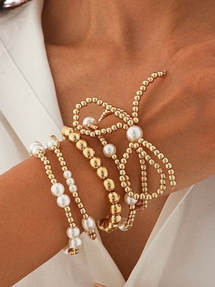 Gold and pearl beaded bracelets on a person's wrist with a white background