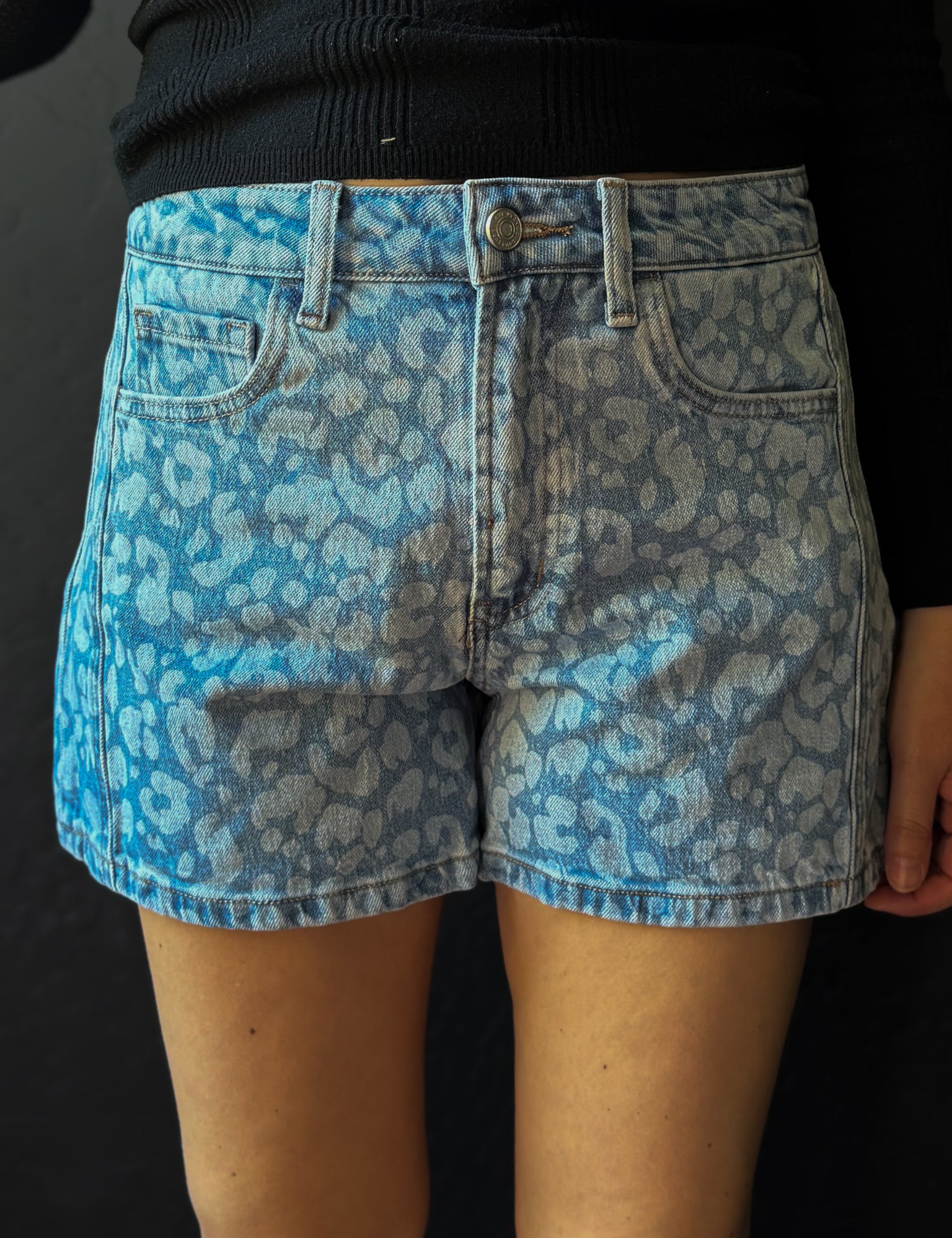 Blue leopard print denim shorts worn by a person on a black background